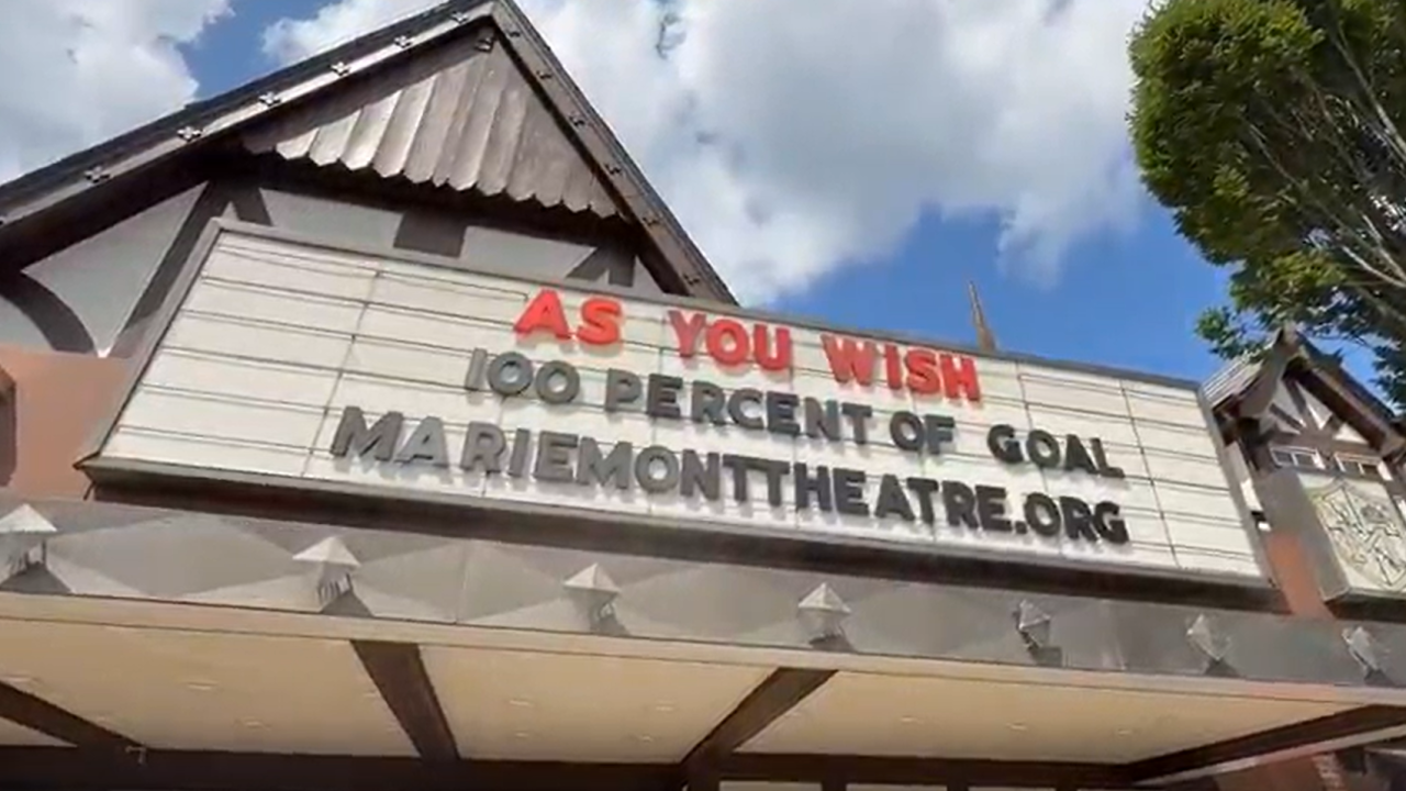 Historic theatre marquee reading 'As You Wish 100 Percent of Goal' against a partly cloudy sky.
