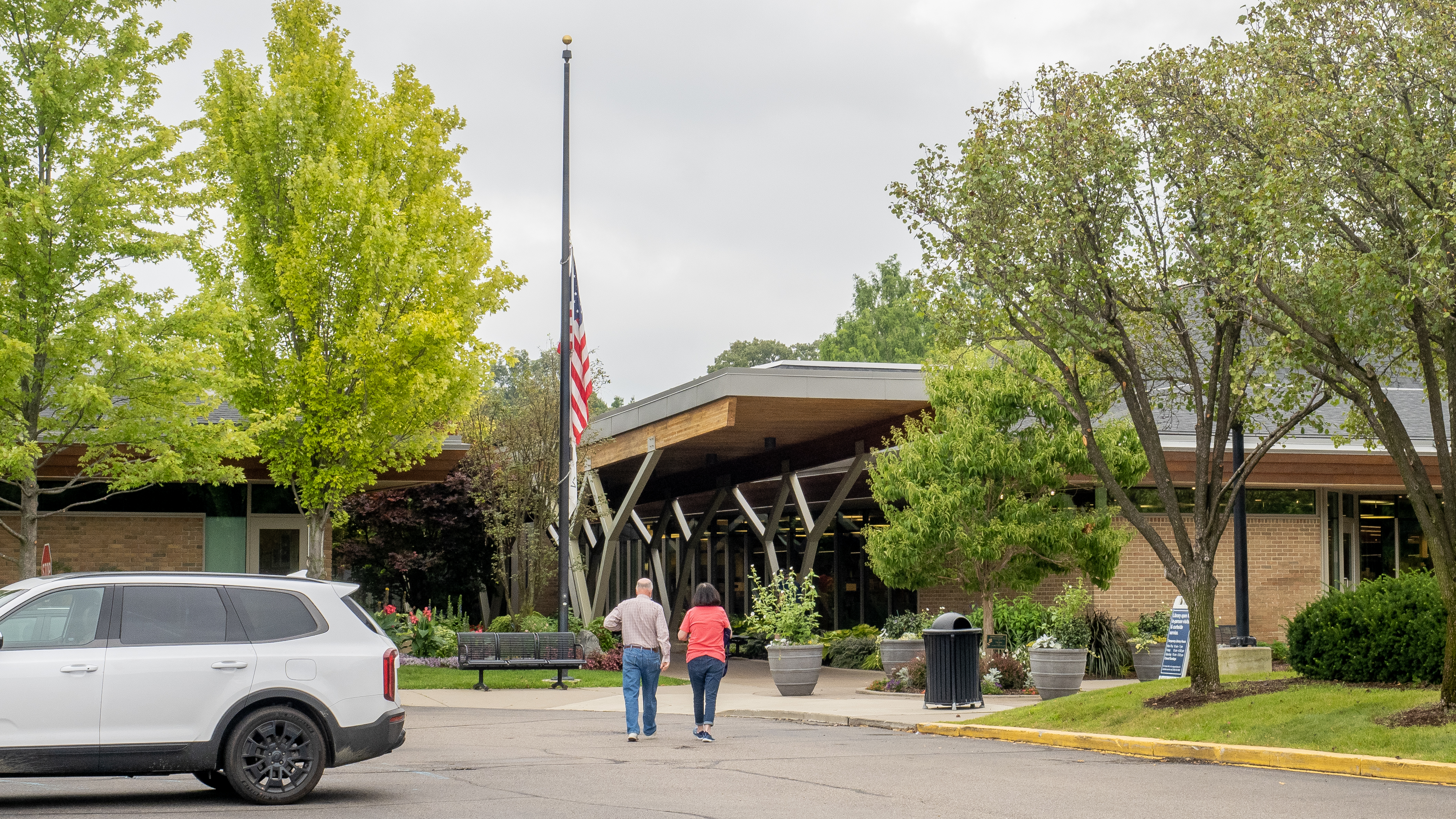 Exterior of a mid-century modern public library with a flagpole and visitors near the entrance.