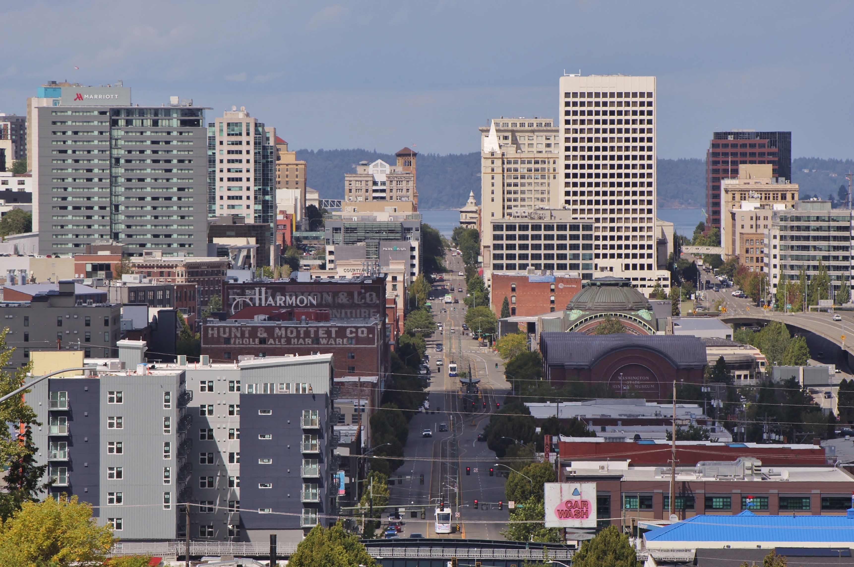 Downtown Tacoma skyline stretching along a wide urban avenue on a partly cloudy day.