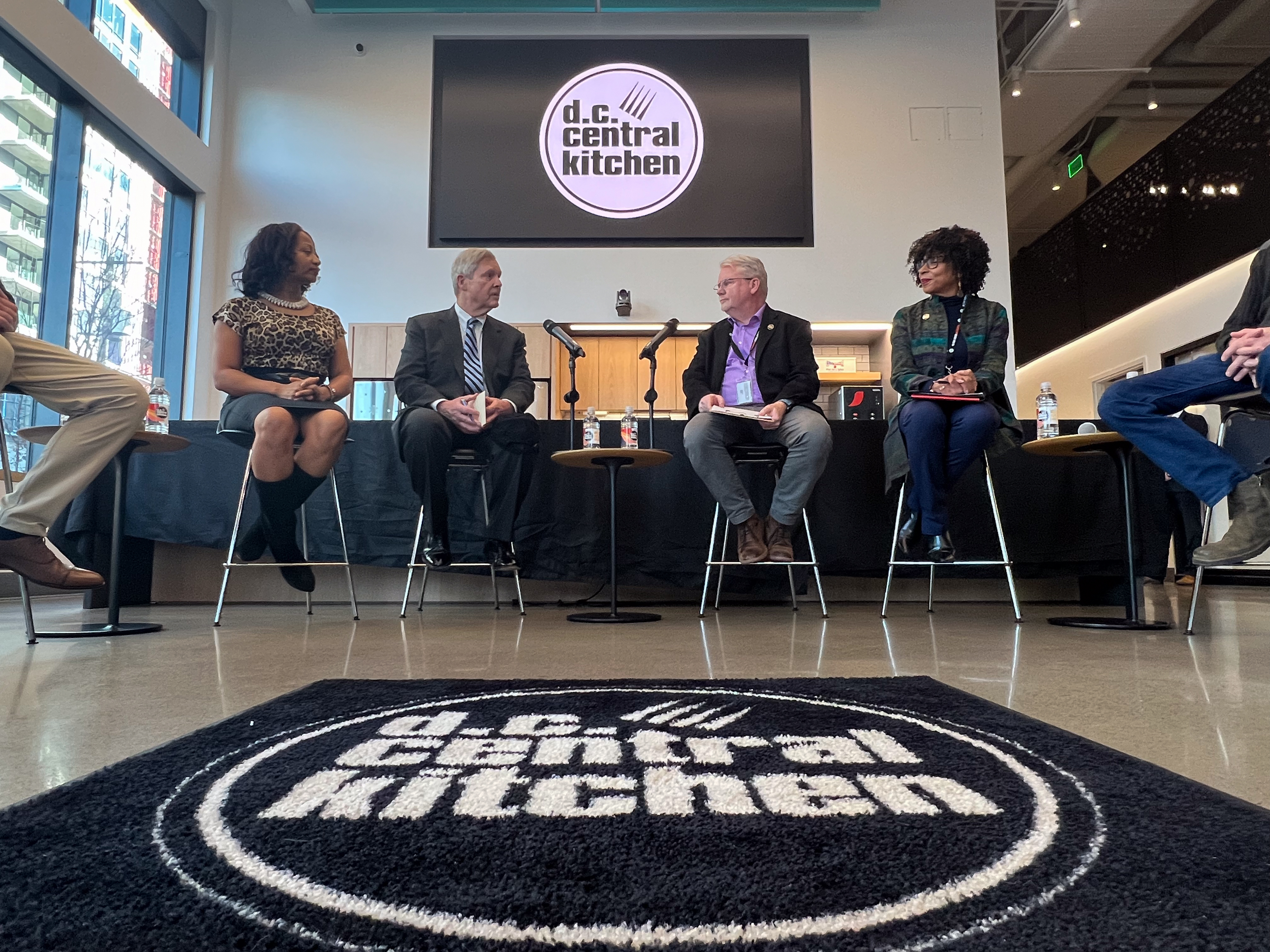 Four people seated on stools in a panel discussion in front of a DC Central Kitchen logo sign.