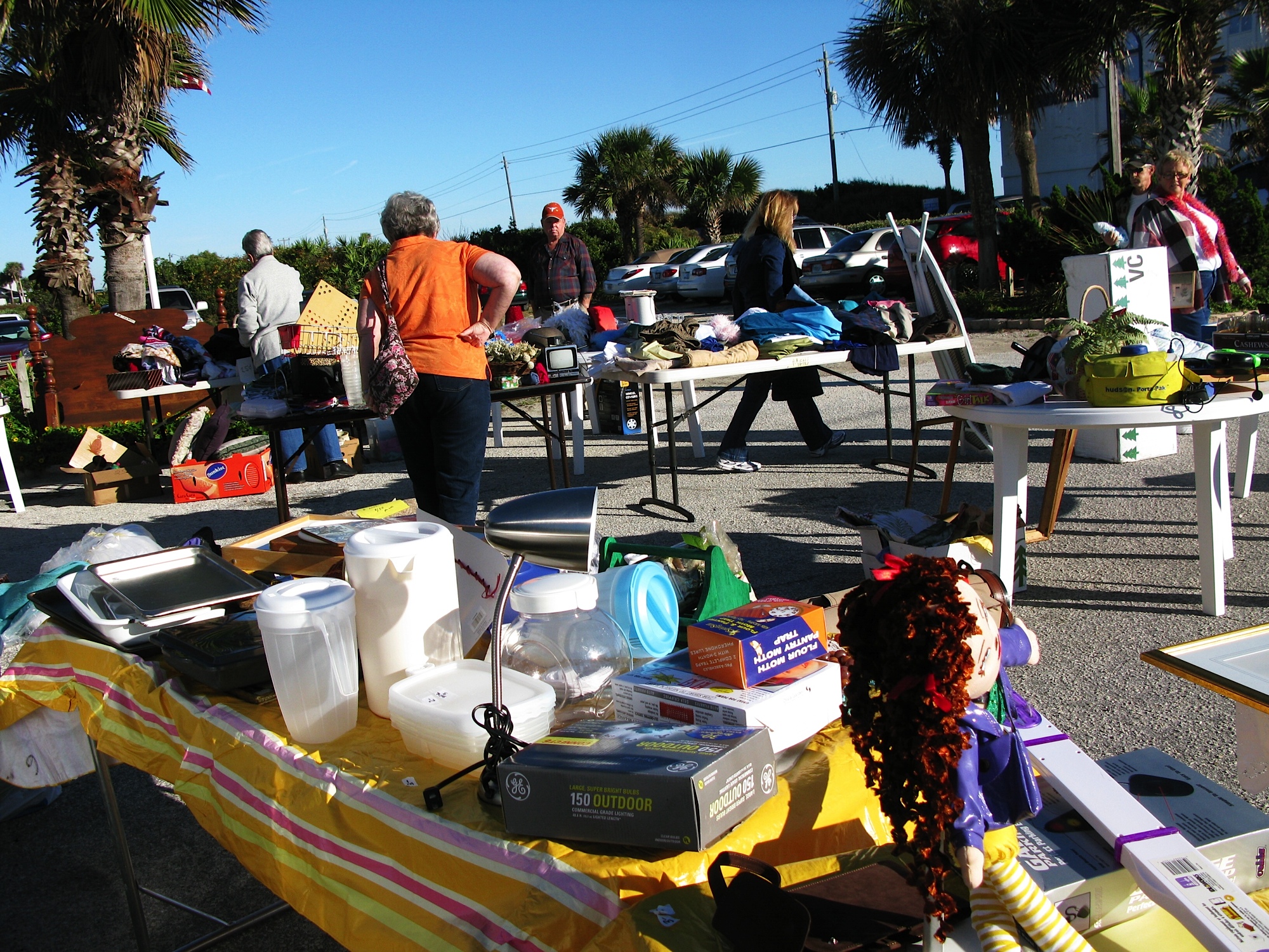 Shoppers browse folding tables of household items at an outdoor yard sale.
