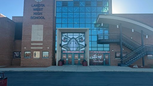 Brick high school building exterior with glass entrance doors and a welcome sign.