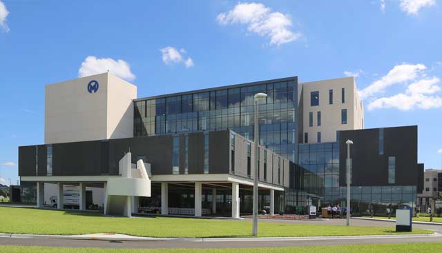 Modern multi-story medical building with glass curtain walls and a blue M logo