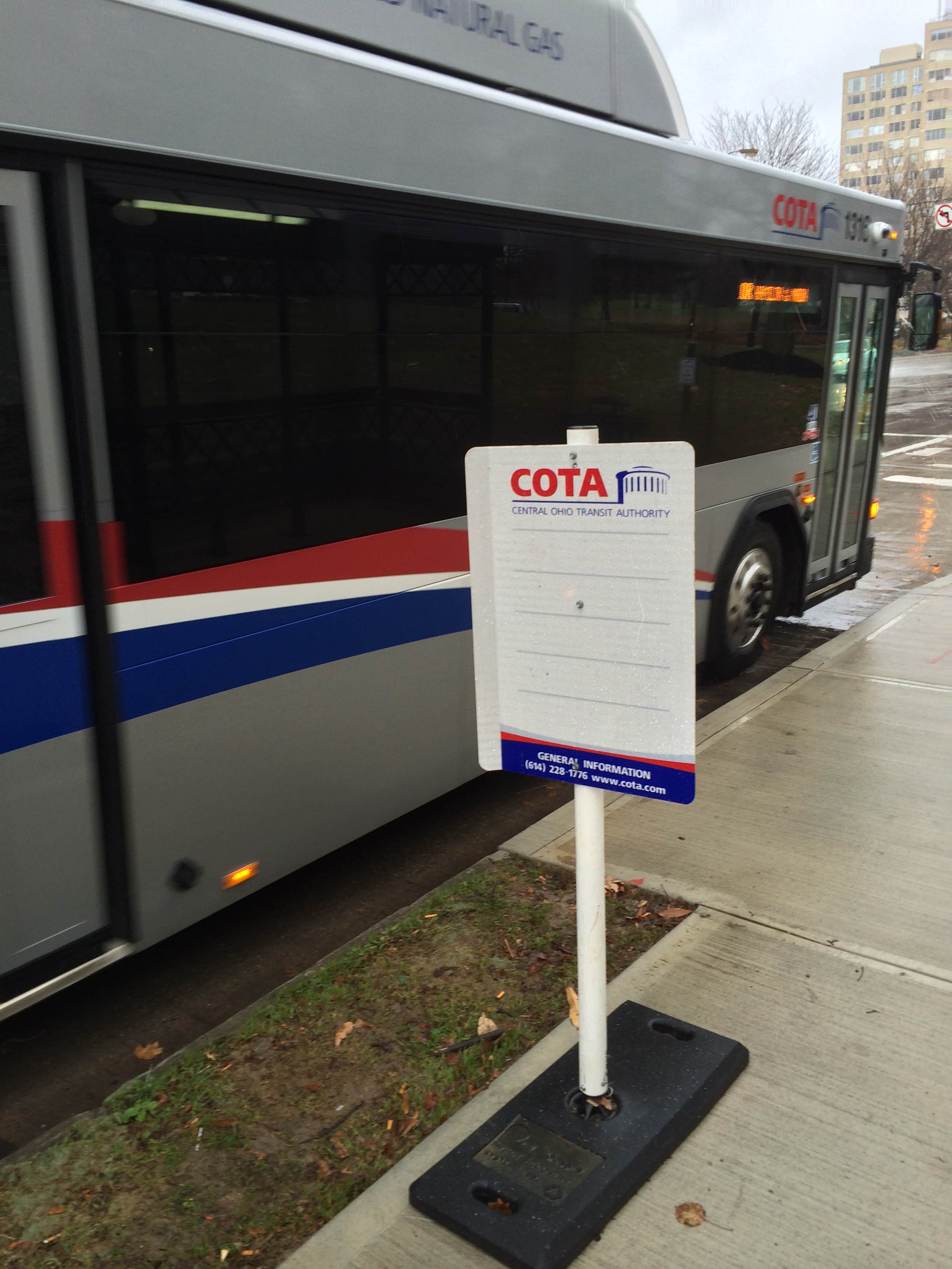 A COTA bus stop sign on a city street with a COTA bus approaching behind it.