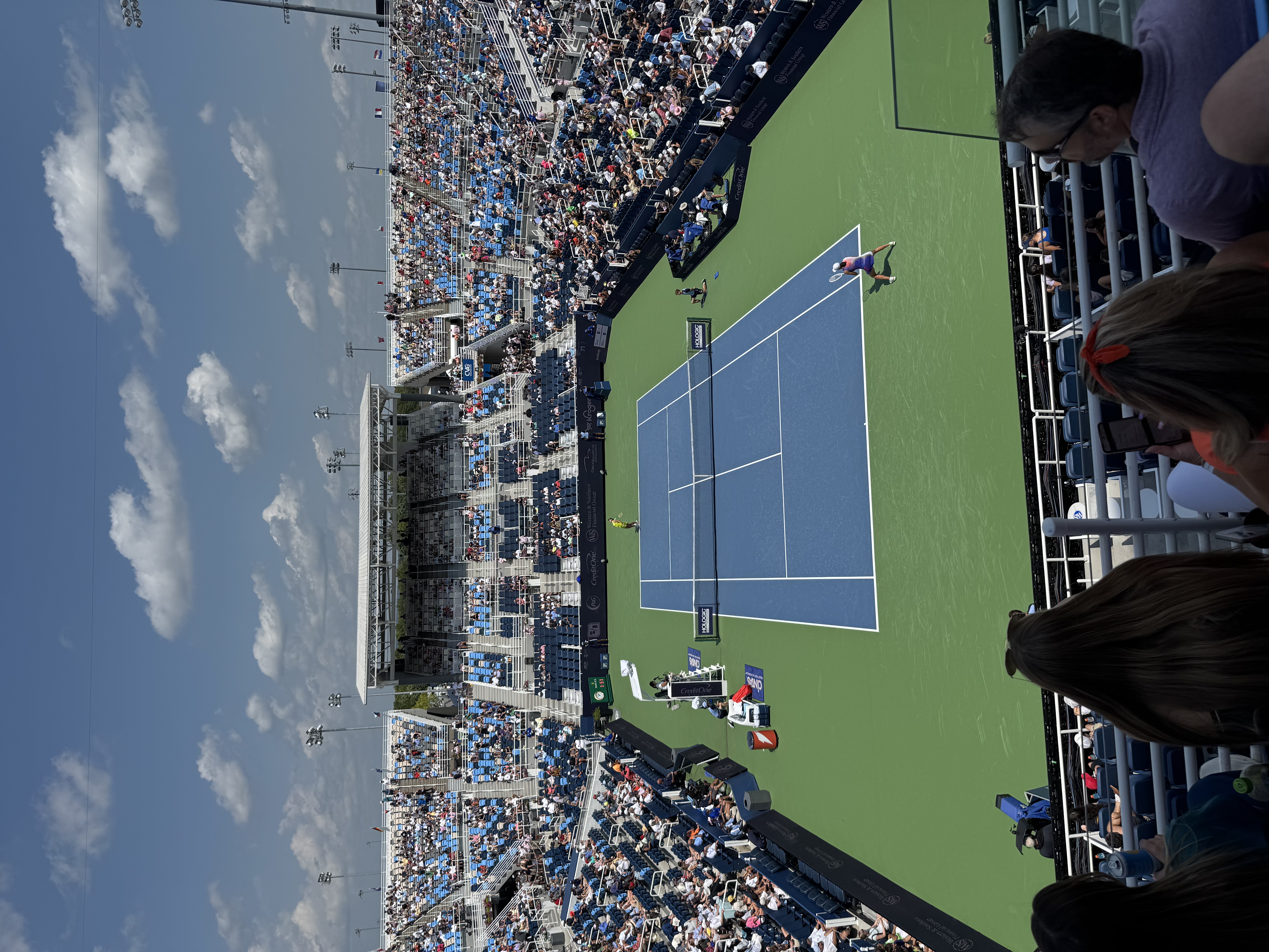 Aerial view of a packed tennis stadium with two players on a blue hard court.