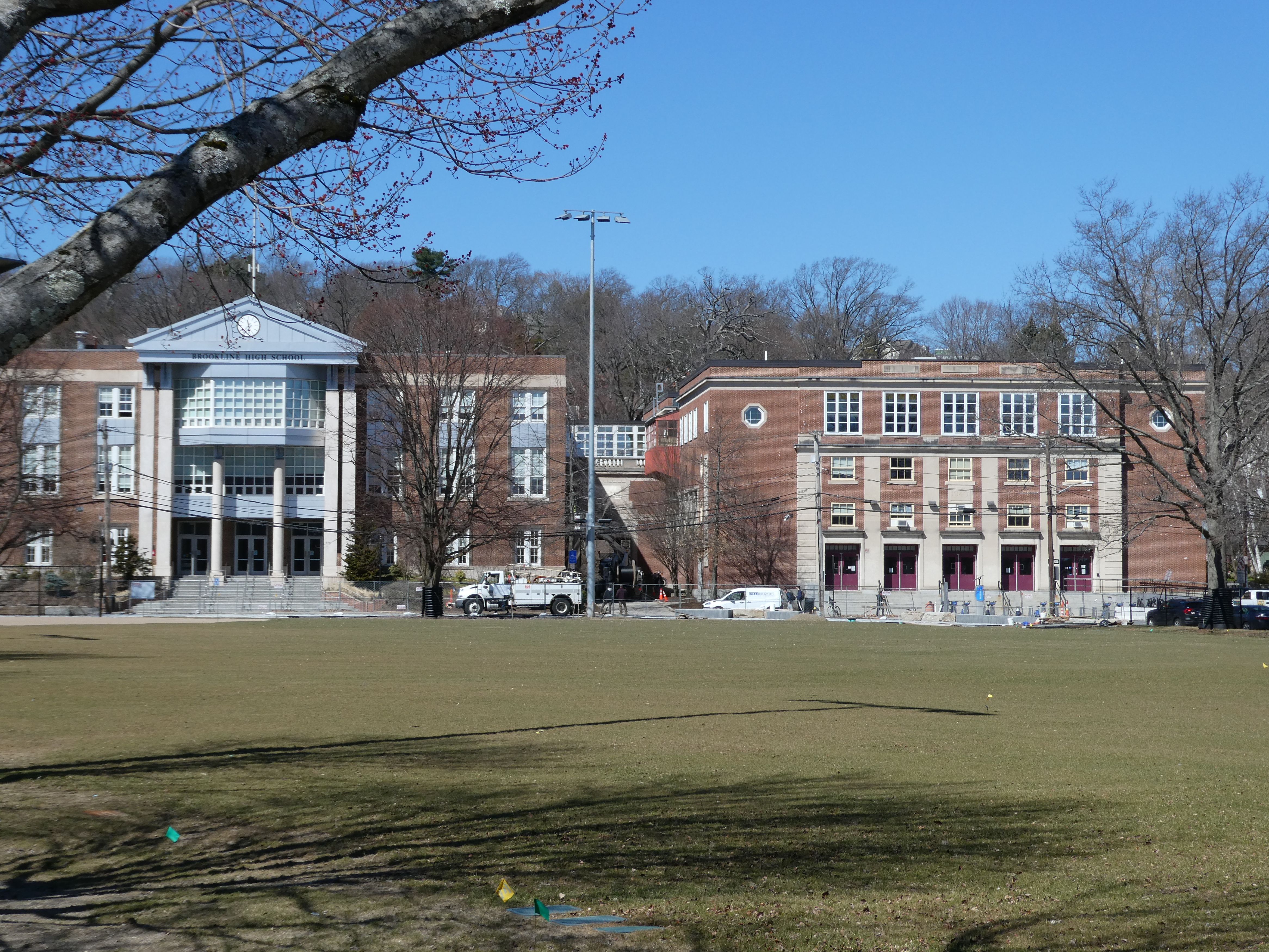 Two connected brick school buildings with a classical portico, seen across a grass field.