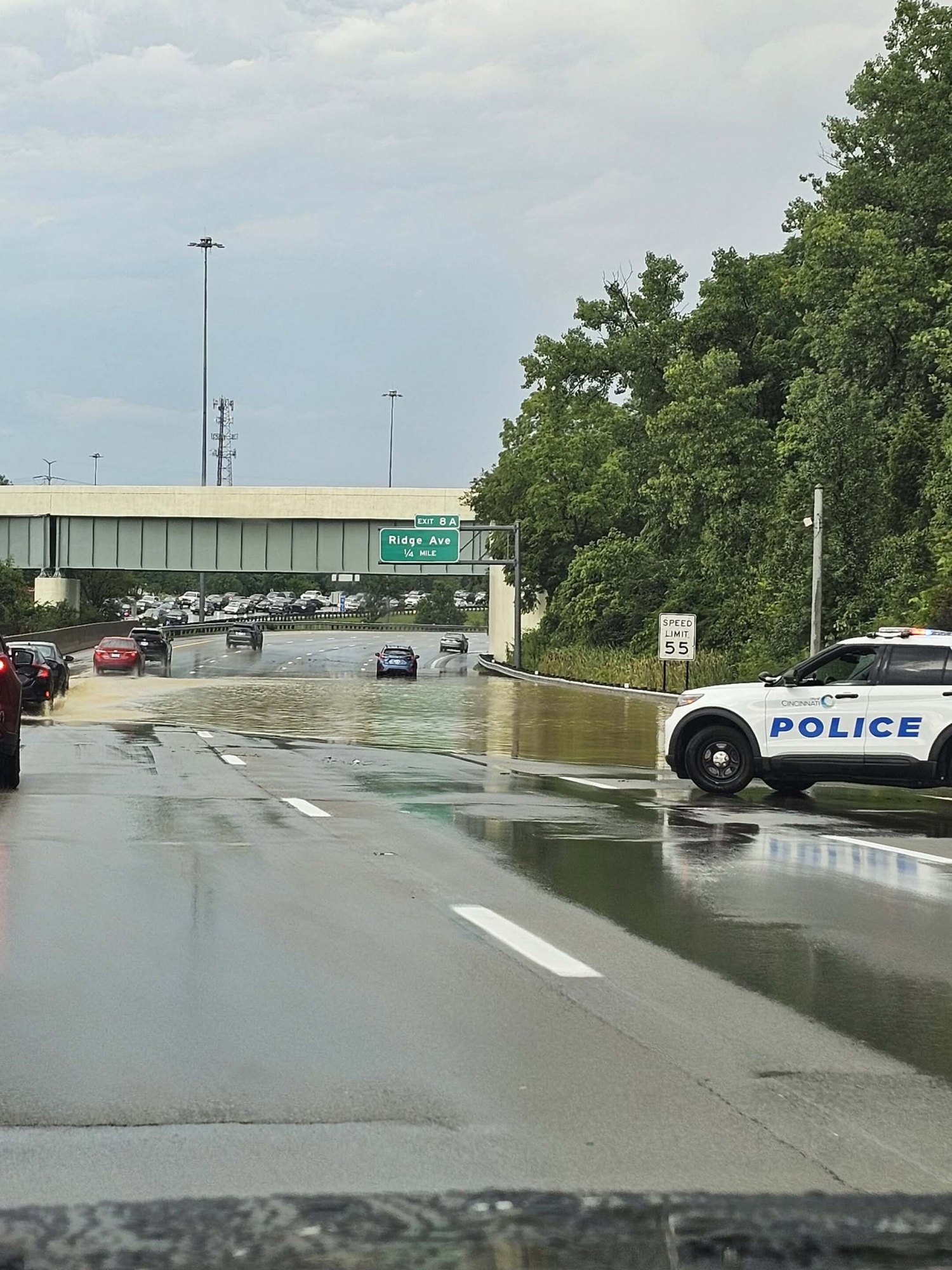 Flooded interstate highway lanes with a police SUV on the shoulder and a Ridge Ave overpass sign visible.