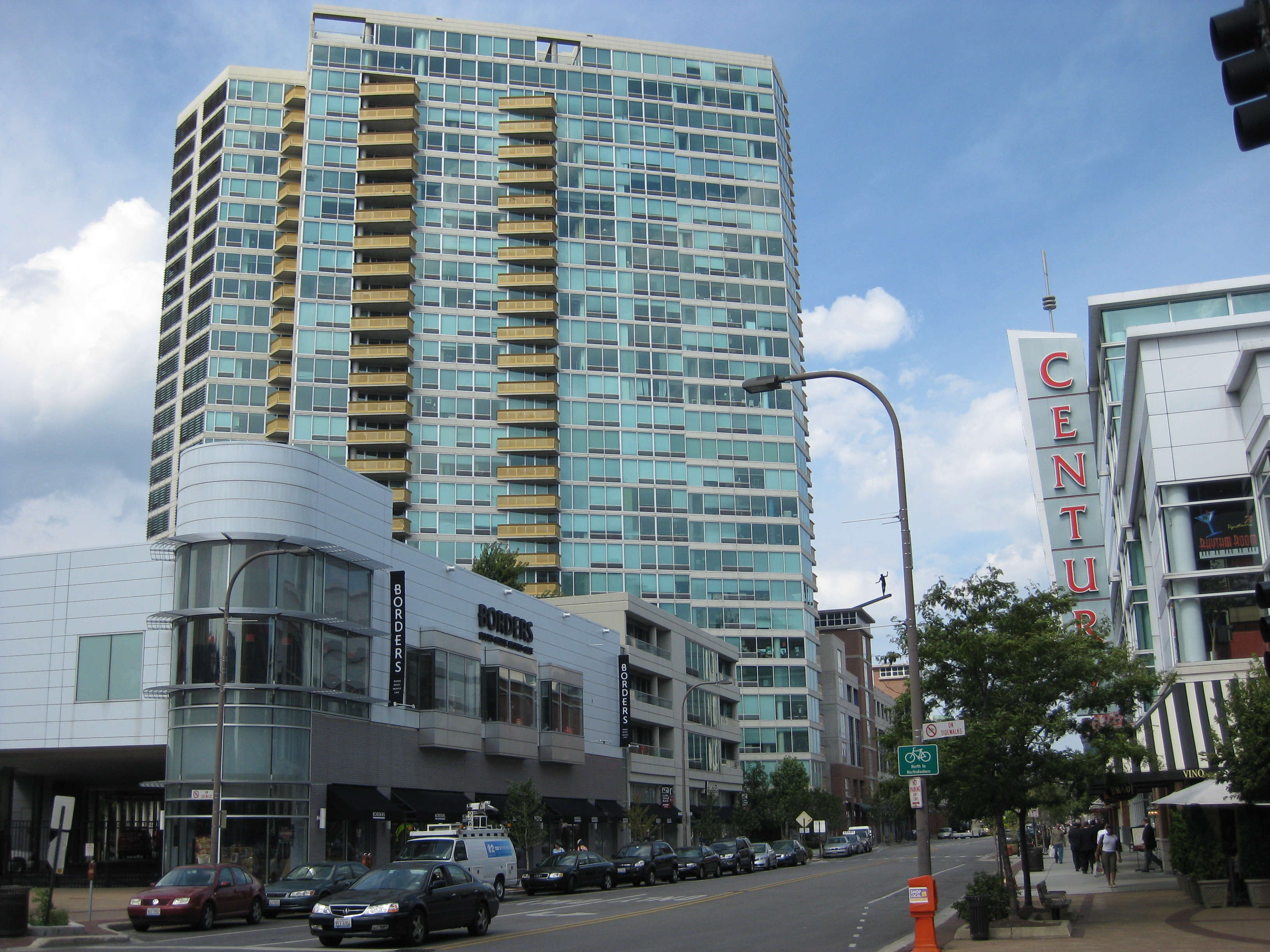 Downtown street with a glass high-rise tower and ground-floor retail storefronts.