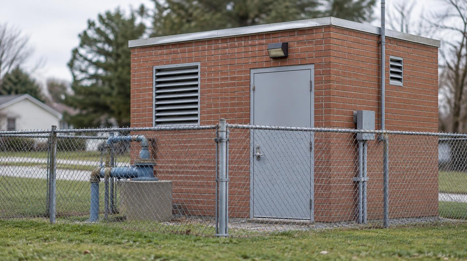 Small brick utility building with metal door and chain-link fence.