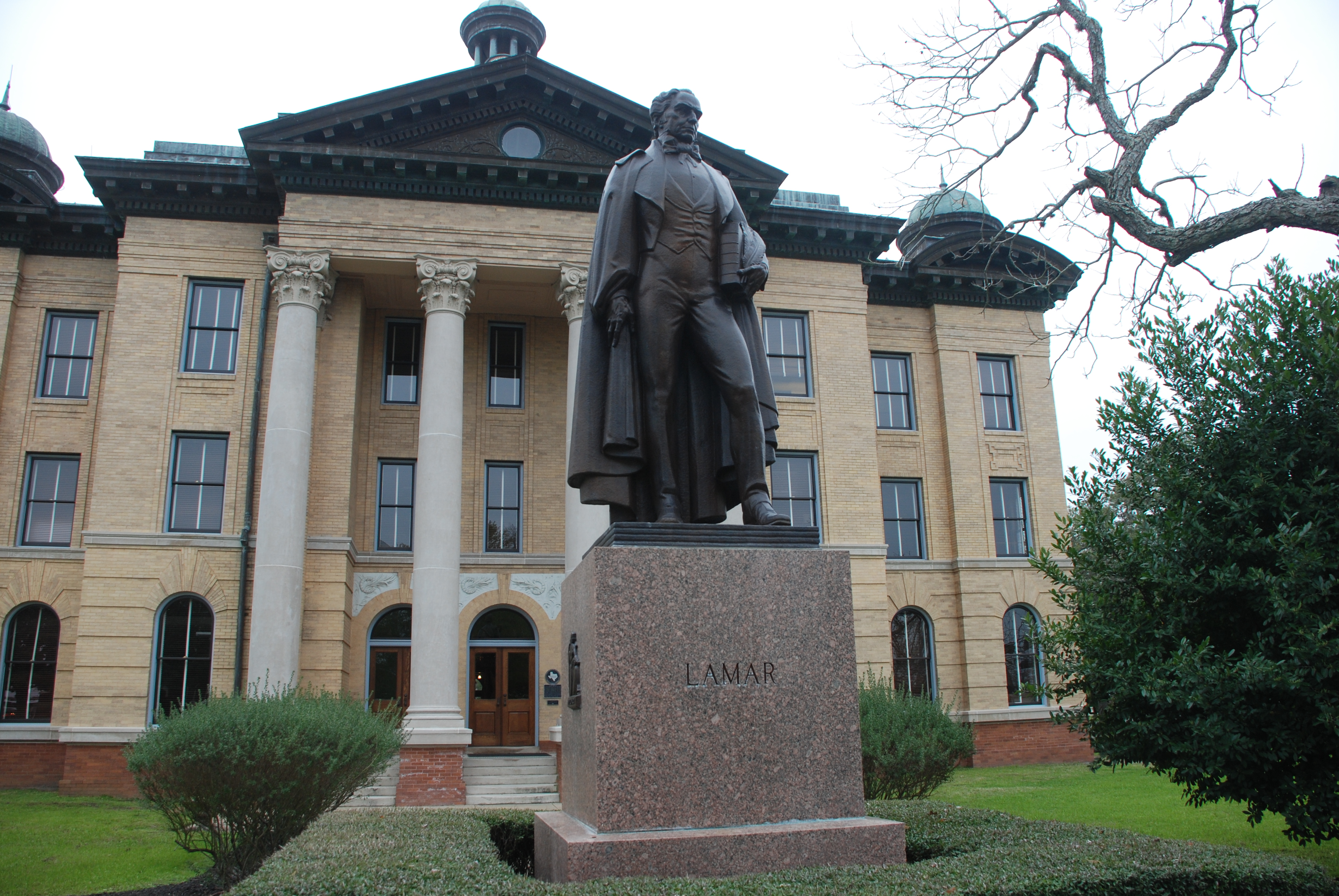 Bronze statue on a granite pedestal in front of a neoclassical courthouse building.
