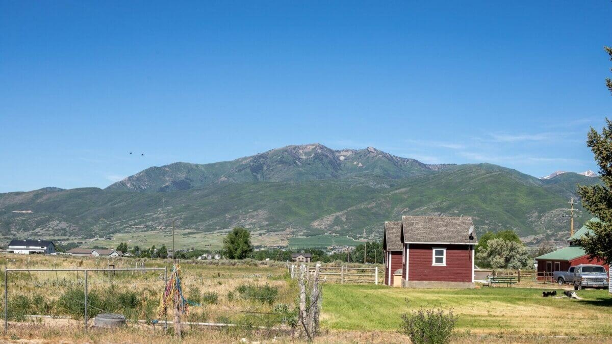 Red barn on a rural farm with fenced fields and mountains in the background.
