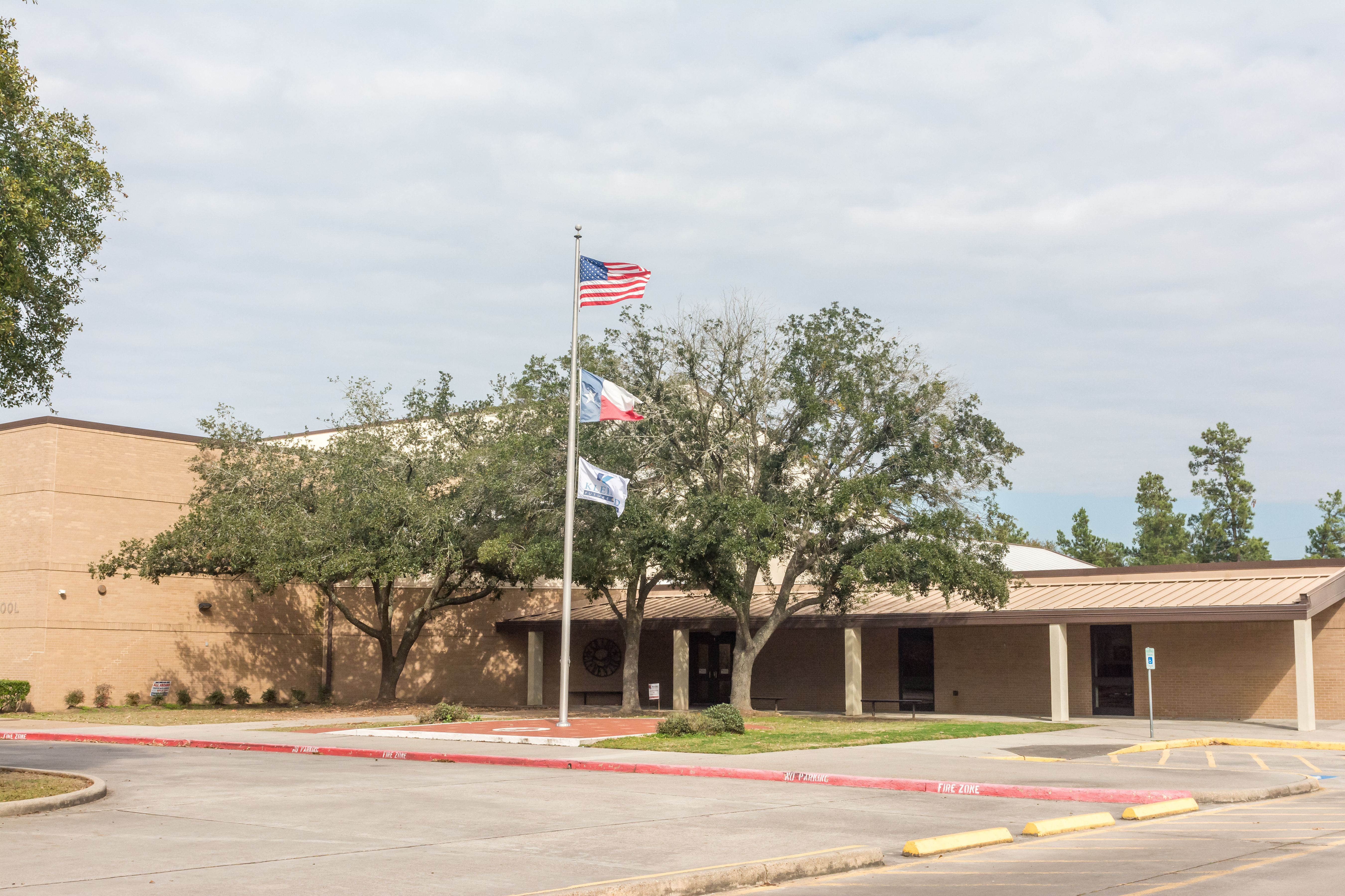 Single-story brick school building with American and Texas flags on a flagpole.
