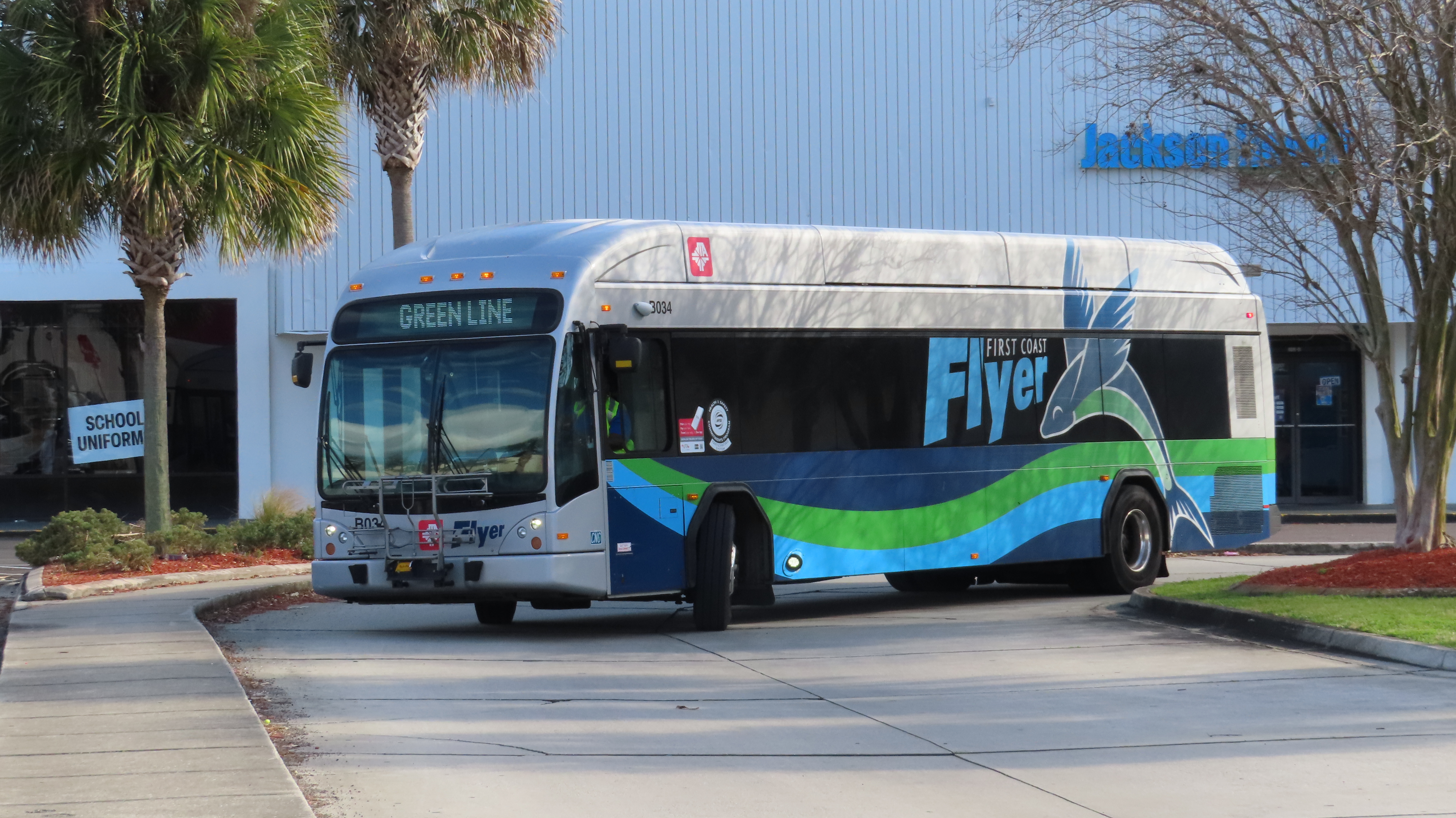 A green and silver JTA First Coast Flyer bus parked at a transit hub at sunset.