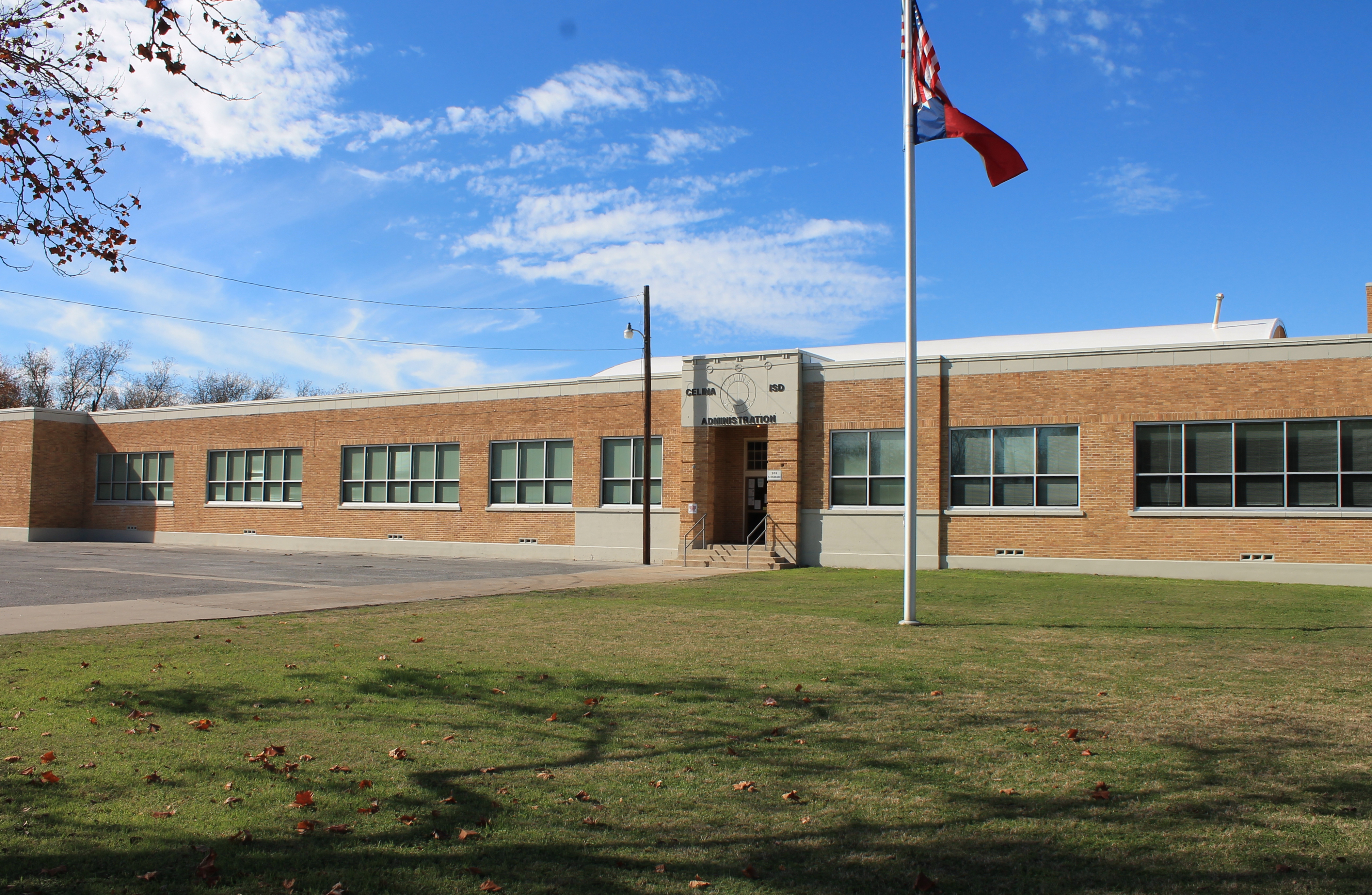 Single-story brick school building with a flagpole and grassy lawn.