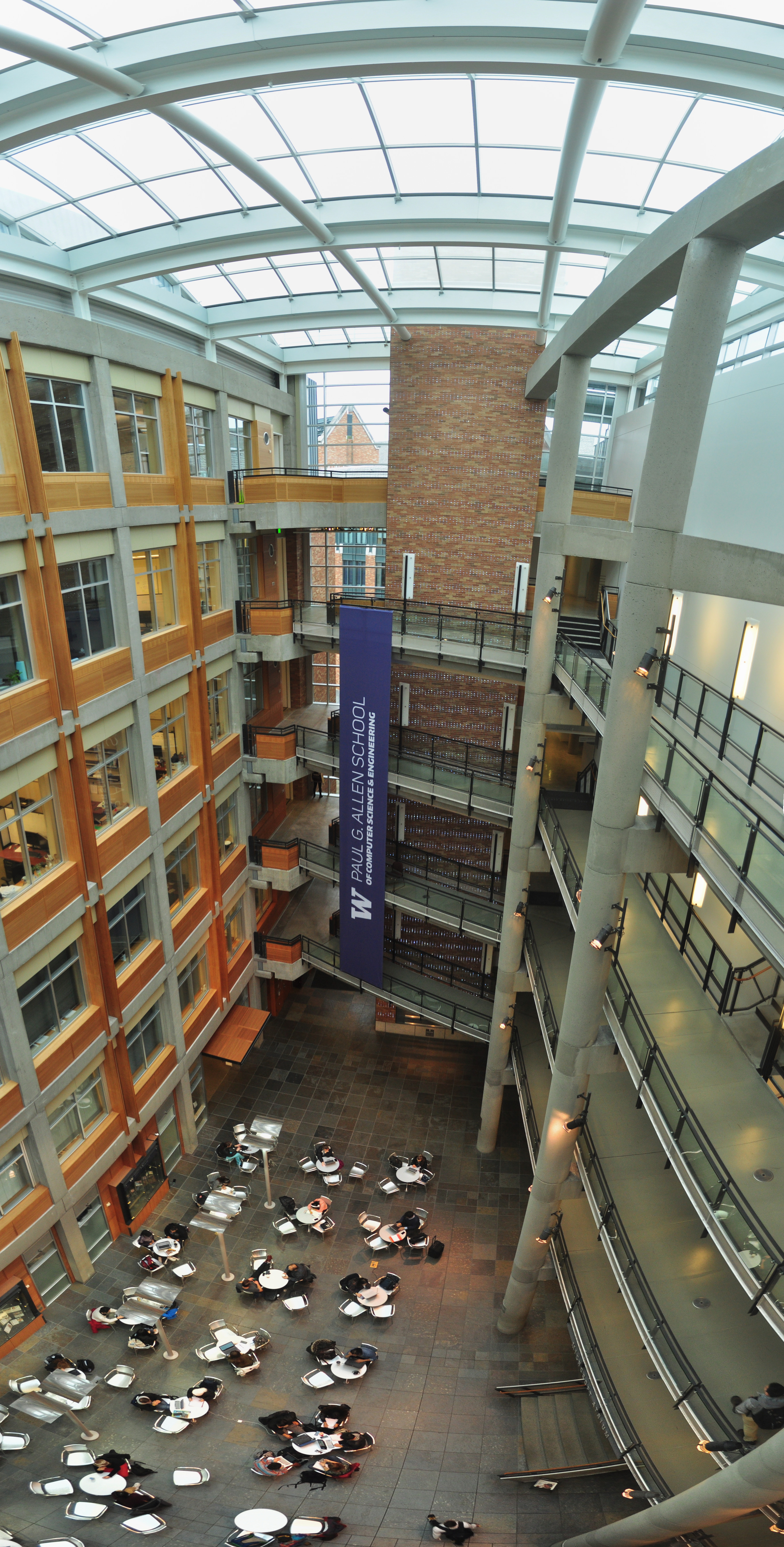 Panoramic atrium interior with glass ceiling, brick walls, multiple balconies, and a blue university banner.