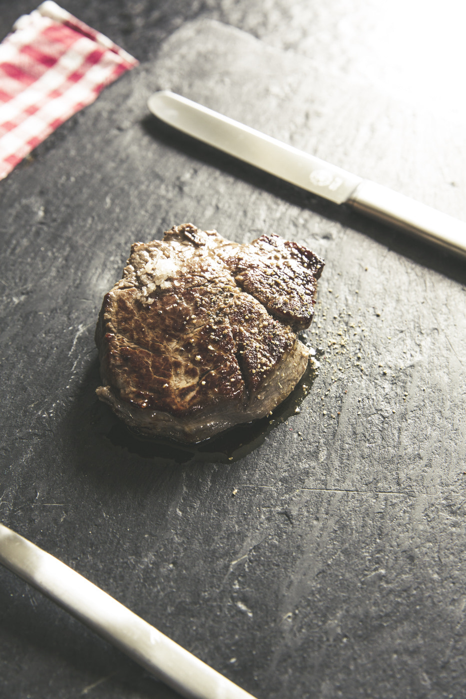 A seared steak on a dark slate surface with a knife beside it.