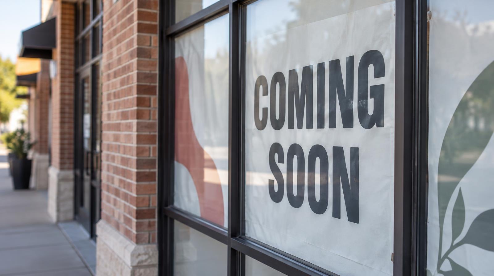 Retail storefront windows covered with paper signage on a brick shopping center building.