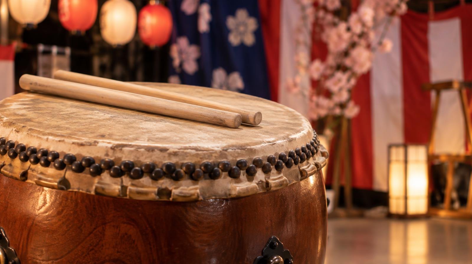 A large taiko drum with two bachi drumsticks resting on top, surrounded by colorful festival decorations.