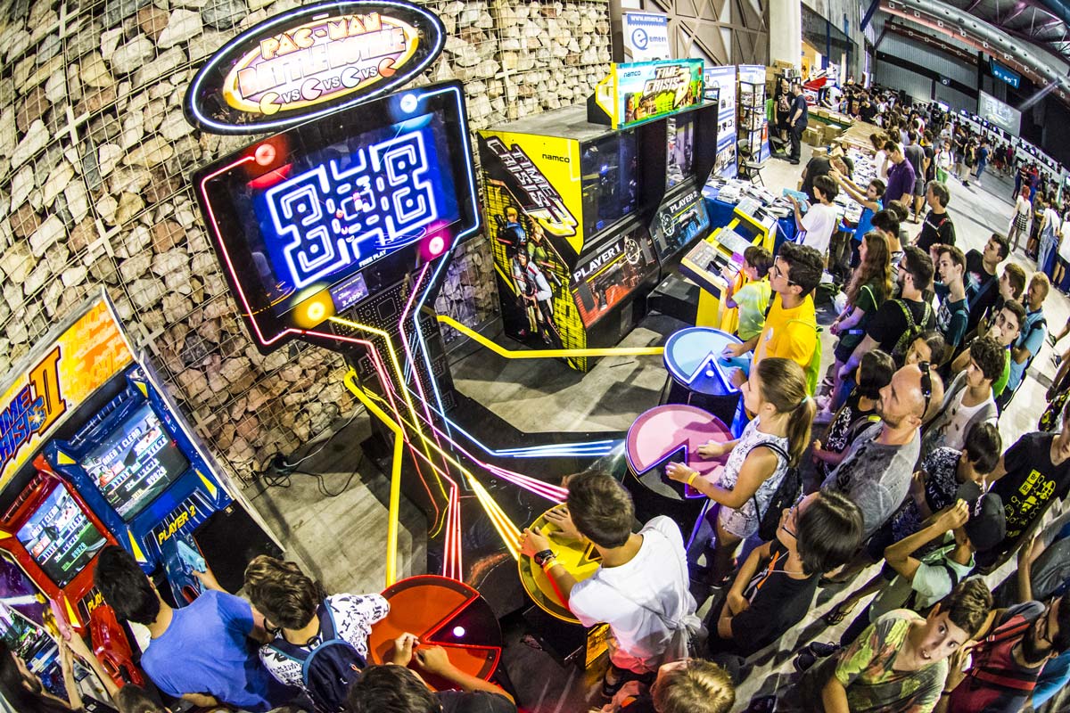 Crowded arcade hall with a prominent Pac-Man cabinet and rows of classic machines.