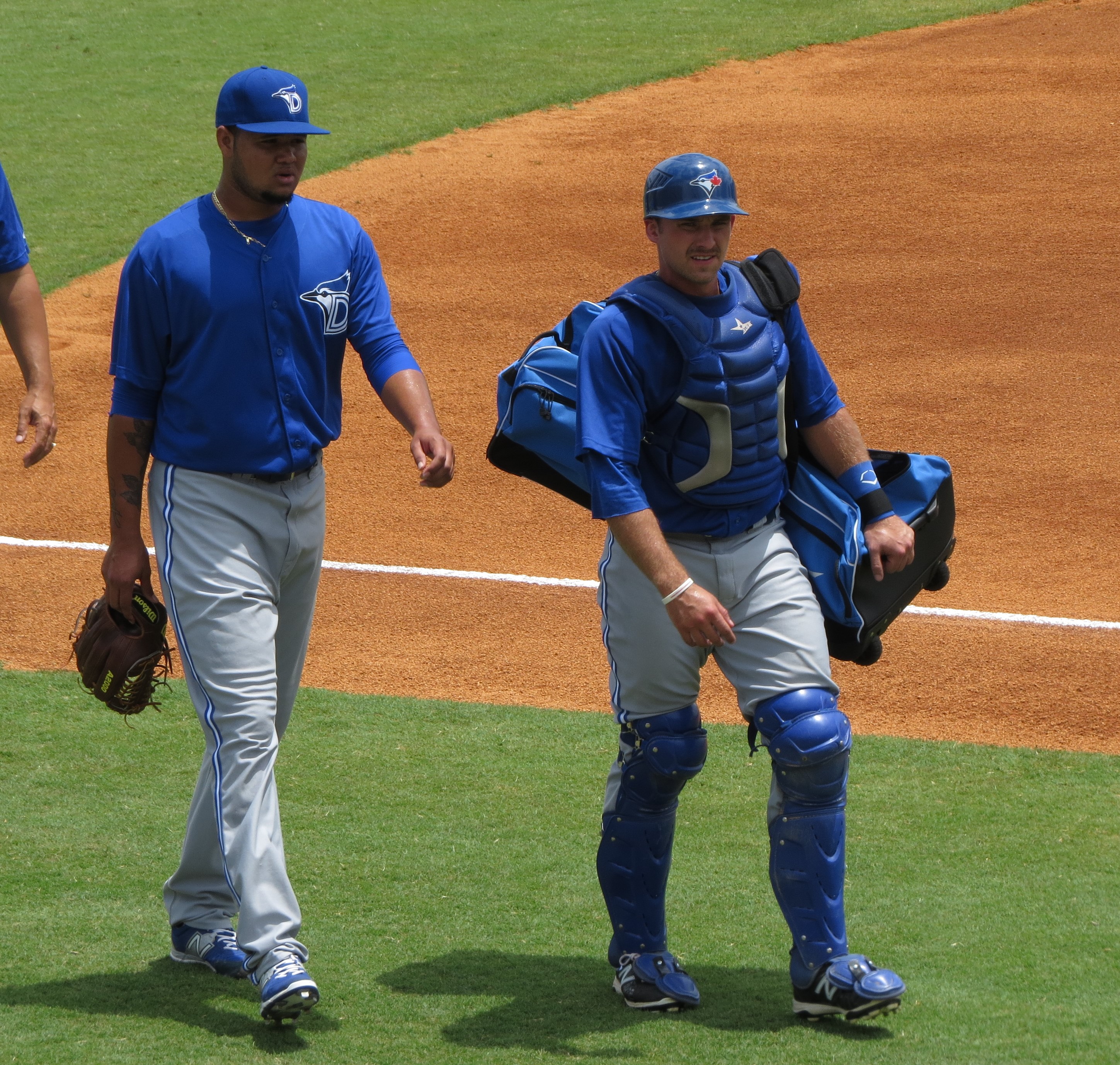 Two baseball players in Dunedin Blue Jays uniforms walking on a field.