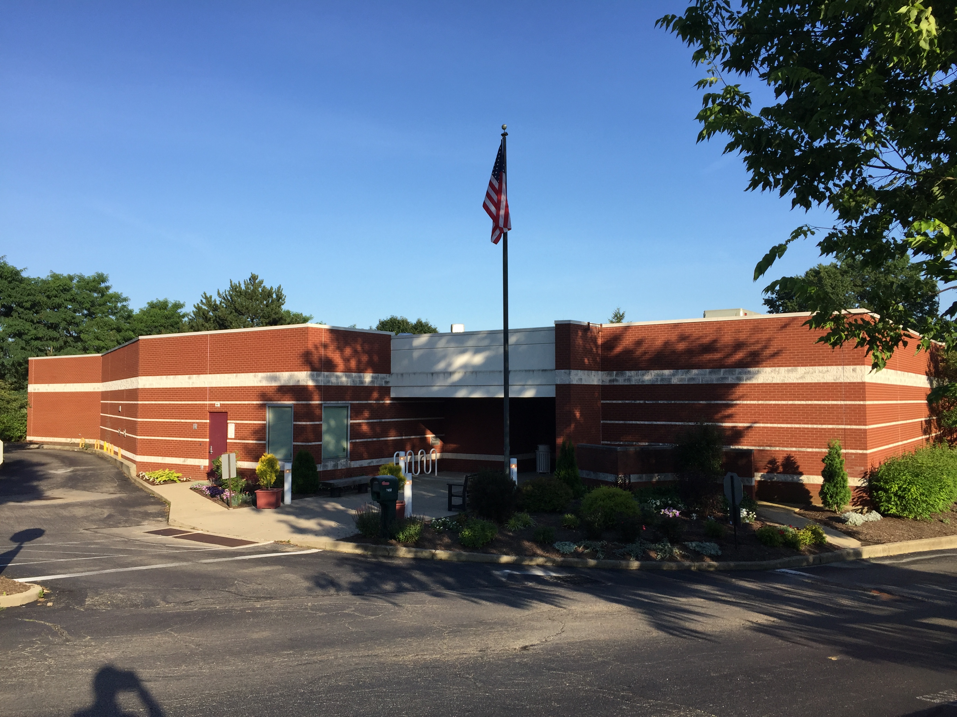 Single-story red brick library building with a flagpole and parking lot in front.