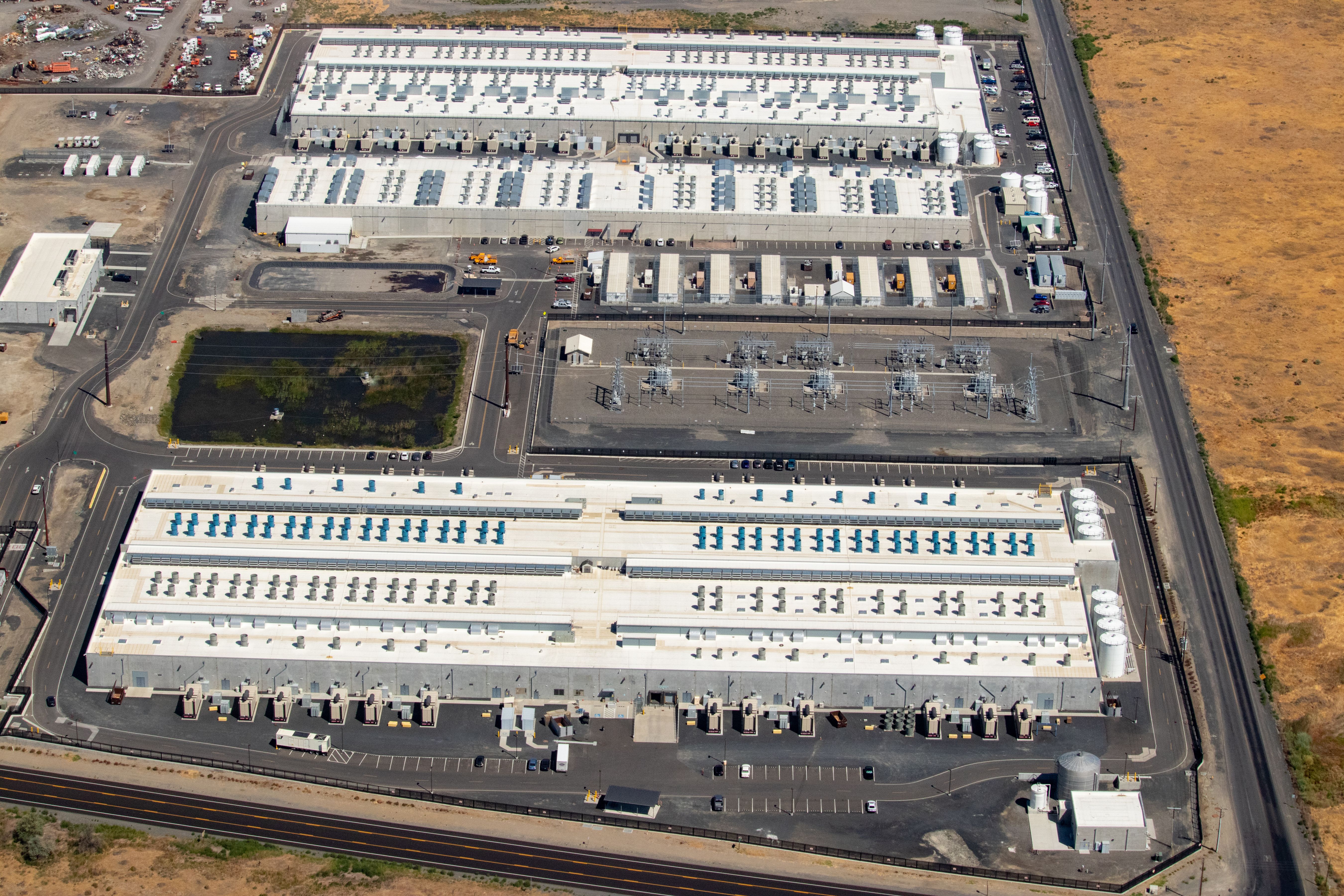 Aerial view of three large data center buildings with rooftop cooling equipment and loading docks.