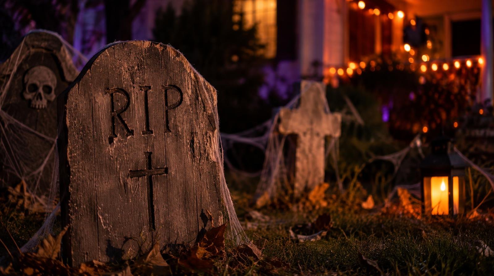 Spooky yard display with wooden tombstones, cobwebs, and orange accent lights at night.