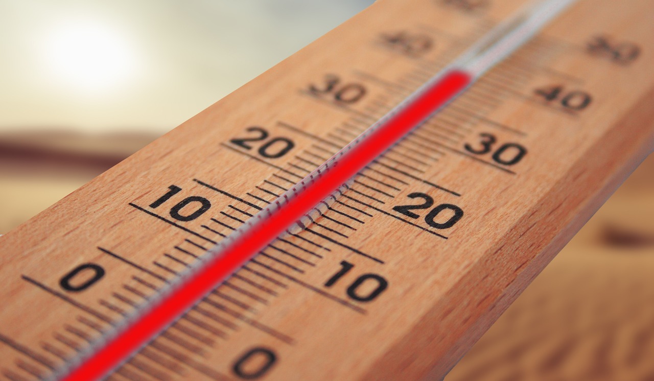 Close-up of a wooden thermometer with the mercury rising, set against a hazy sun in the background.