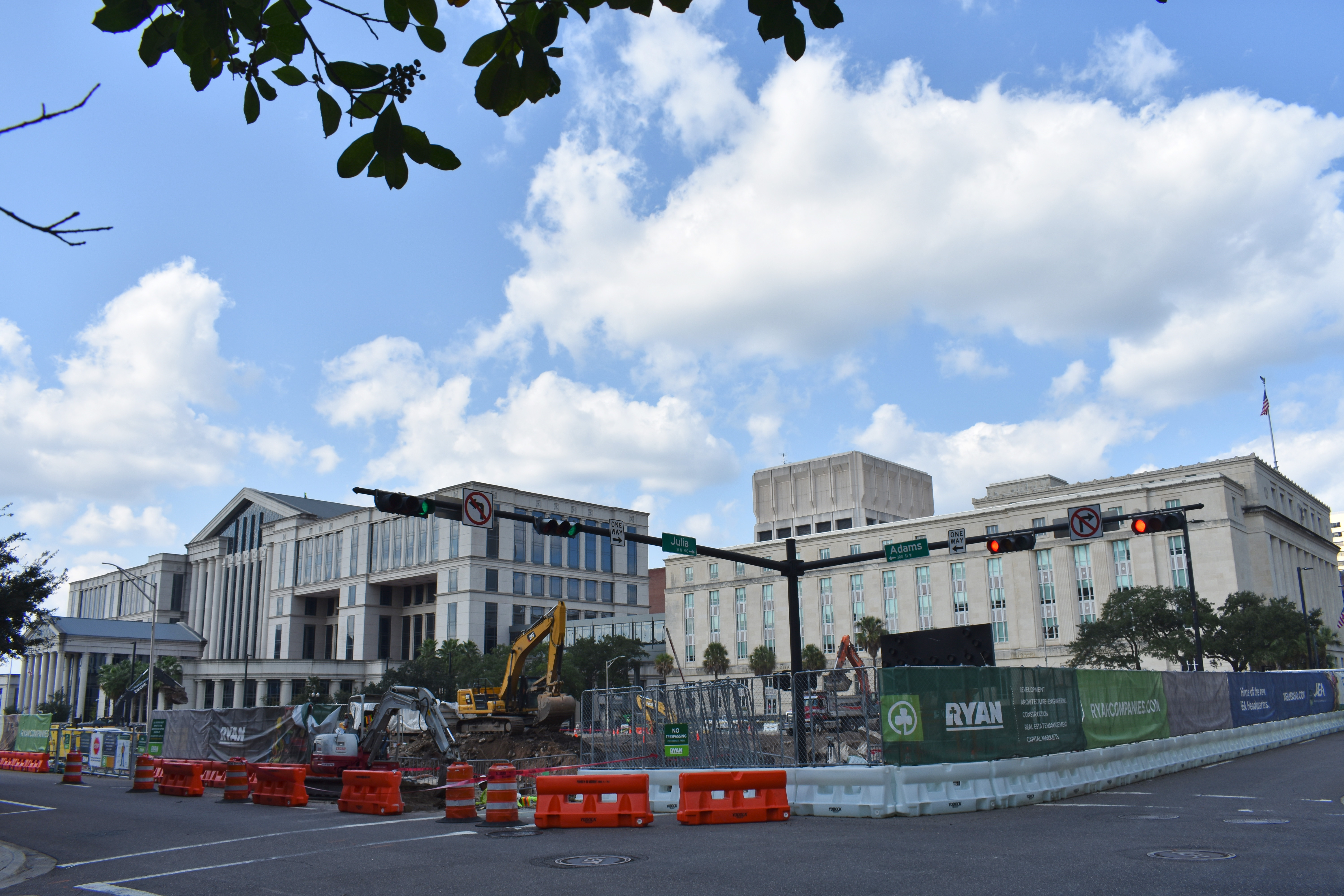 Construction site with excavators and orange barriers in front of large government buildings.