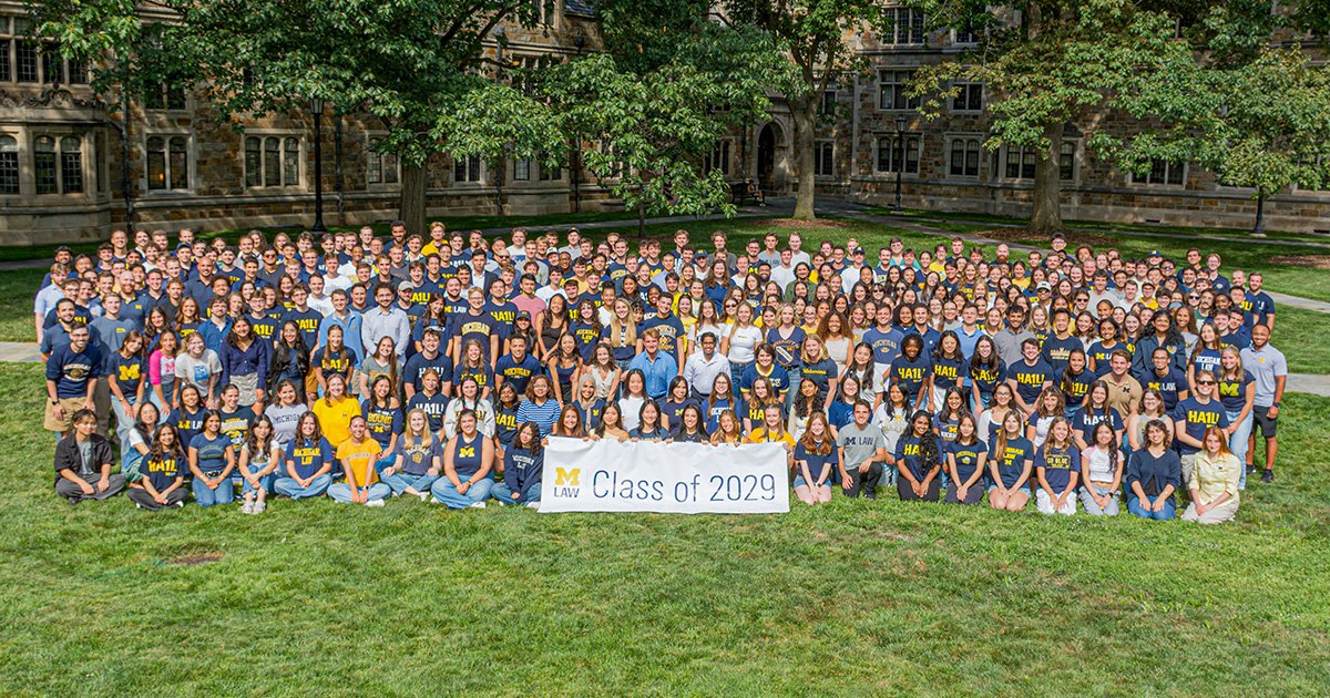Hundreds of students in navy Michigan shirts pose outdoors holding a Class of 2029 banner.