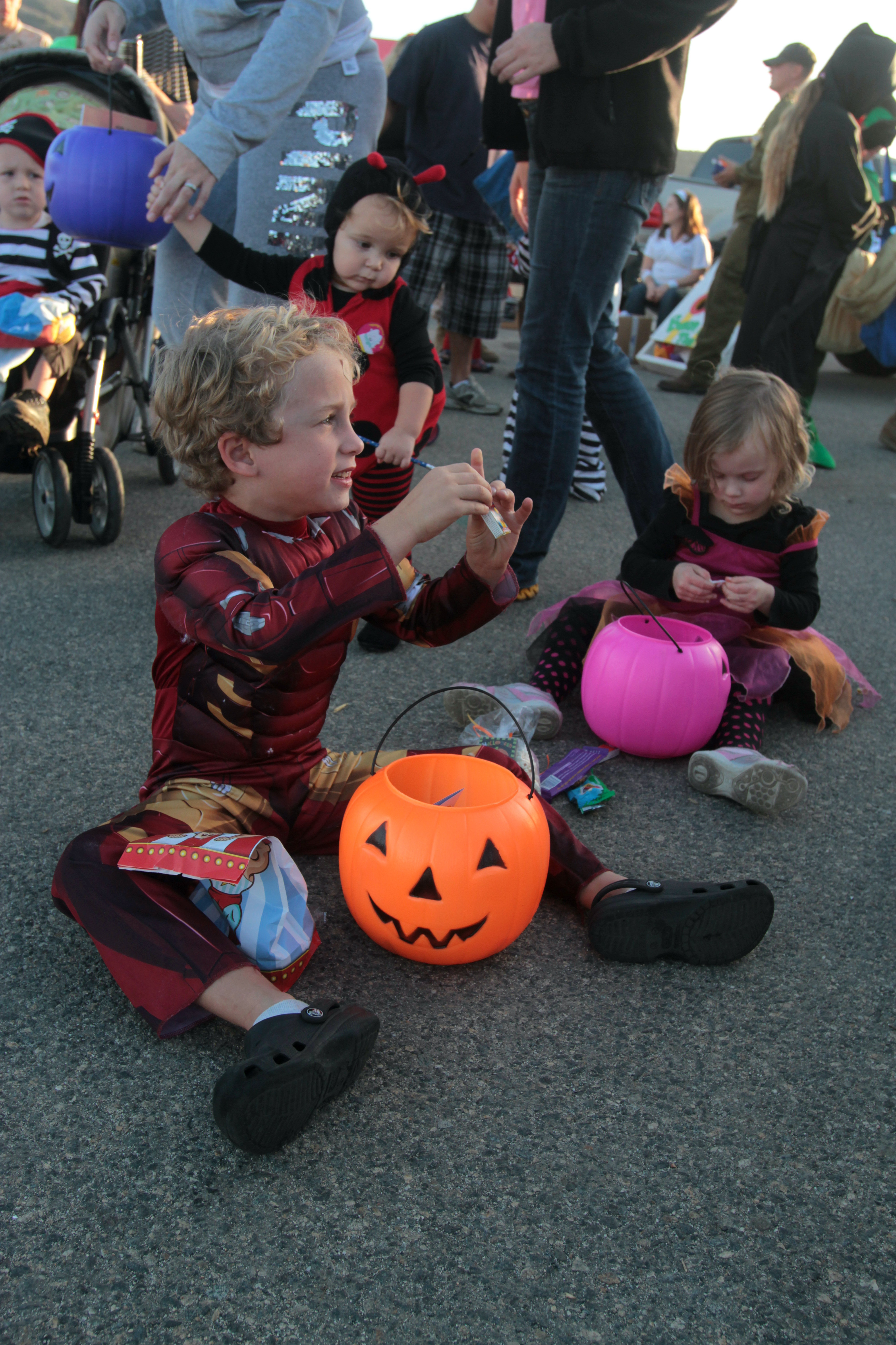 Children in Halloween costumes holding jack-o'-lantern candy buckets at an outdoor event.