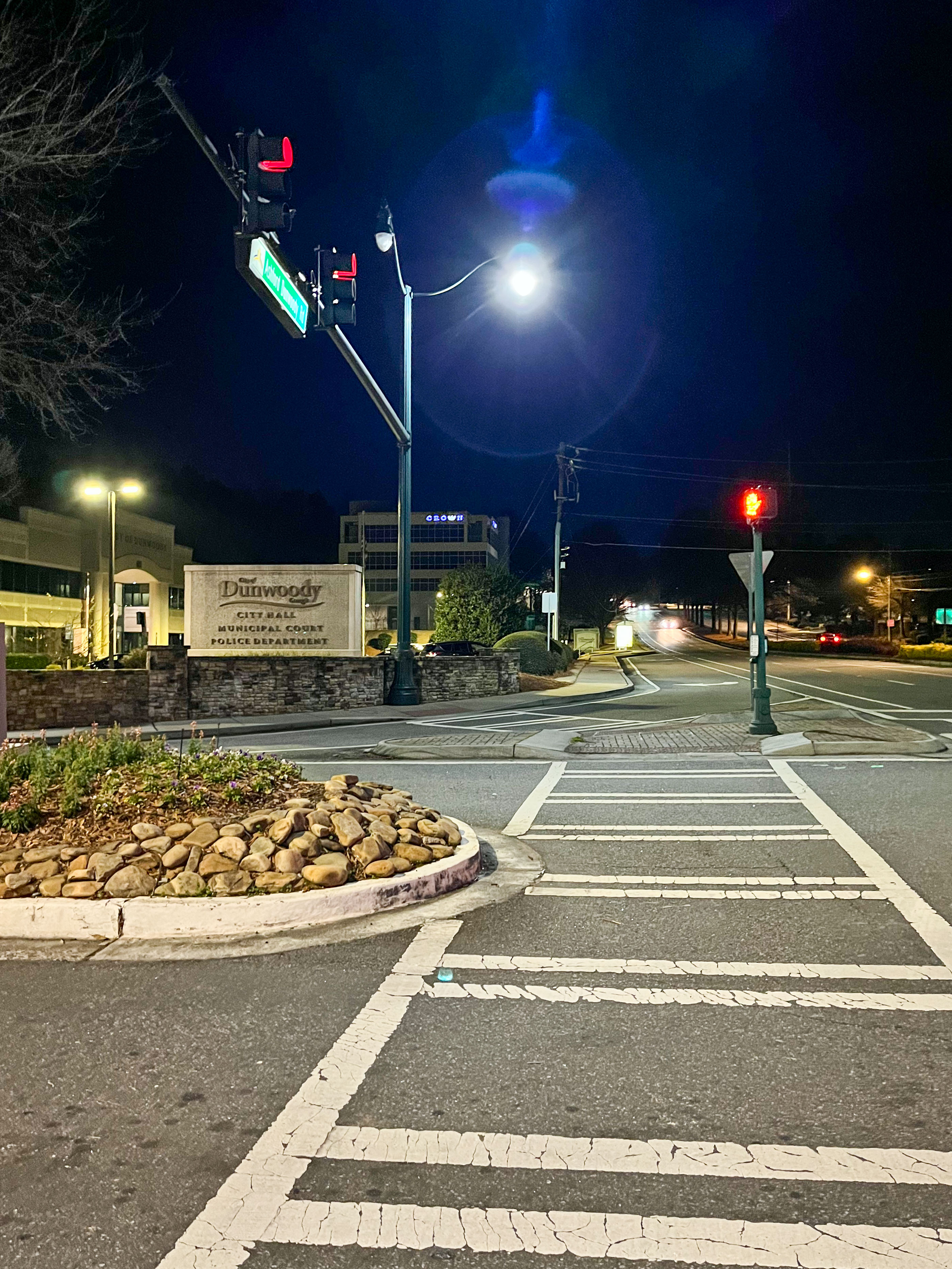 Illuminated Dunwoody City Hall sign at a nighttime intersection.