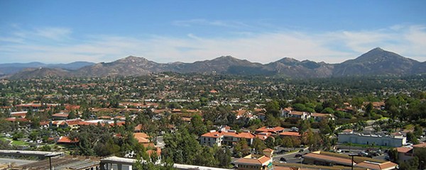 Aerial view of a suburban neighborhood with red-tile roofs and mountains behind.