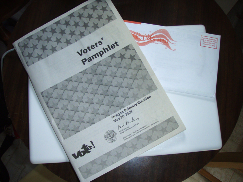 Oregon Voters' Pamphlet booklet resting on a white ballot return envelope on a wooden surface.
