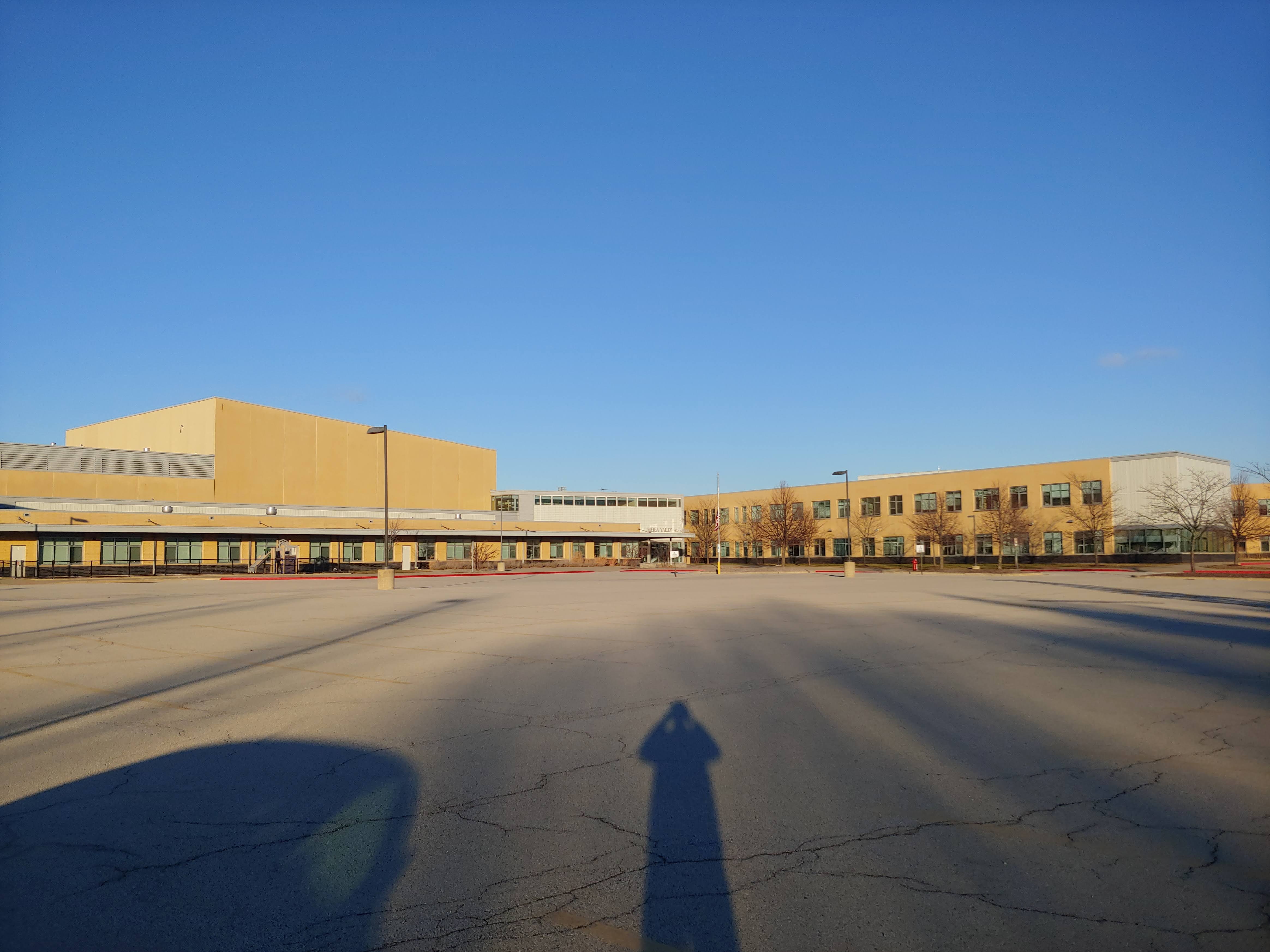Wide view of a large tan brick high school with multiple wings and an open paved area.
