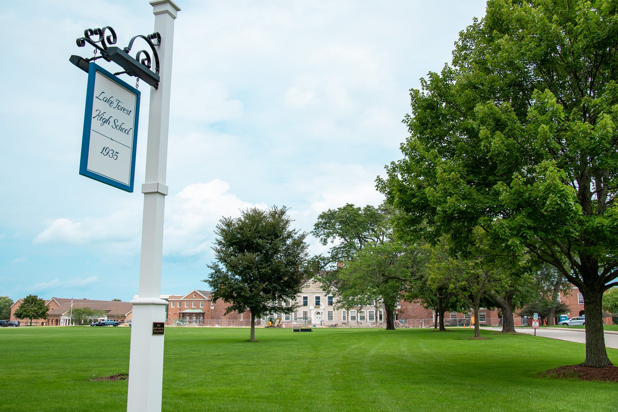 Decorative post sign for a high school on a green lawn with brick buildings behind.