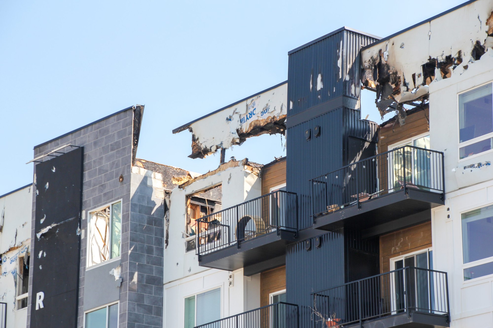 Multi-story apartment building with collapsed, charred roofline and gutted upper floors.