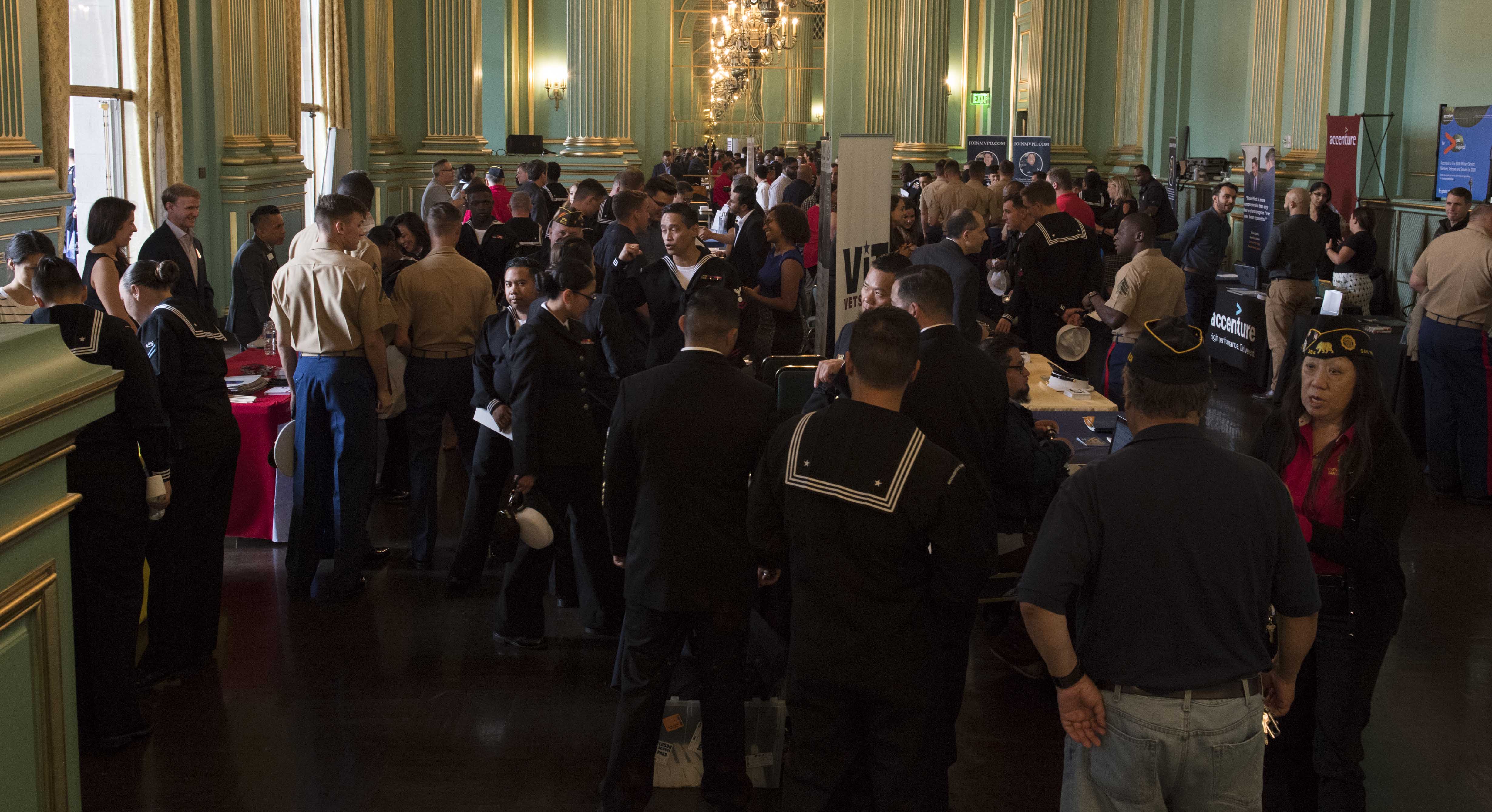 Uniformed military personnel and civilians gather at booths inside a large hall.