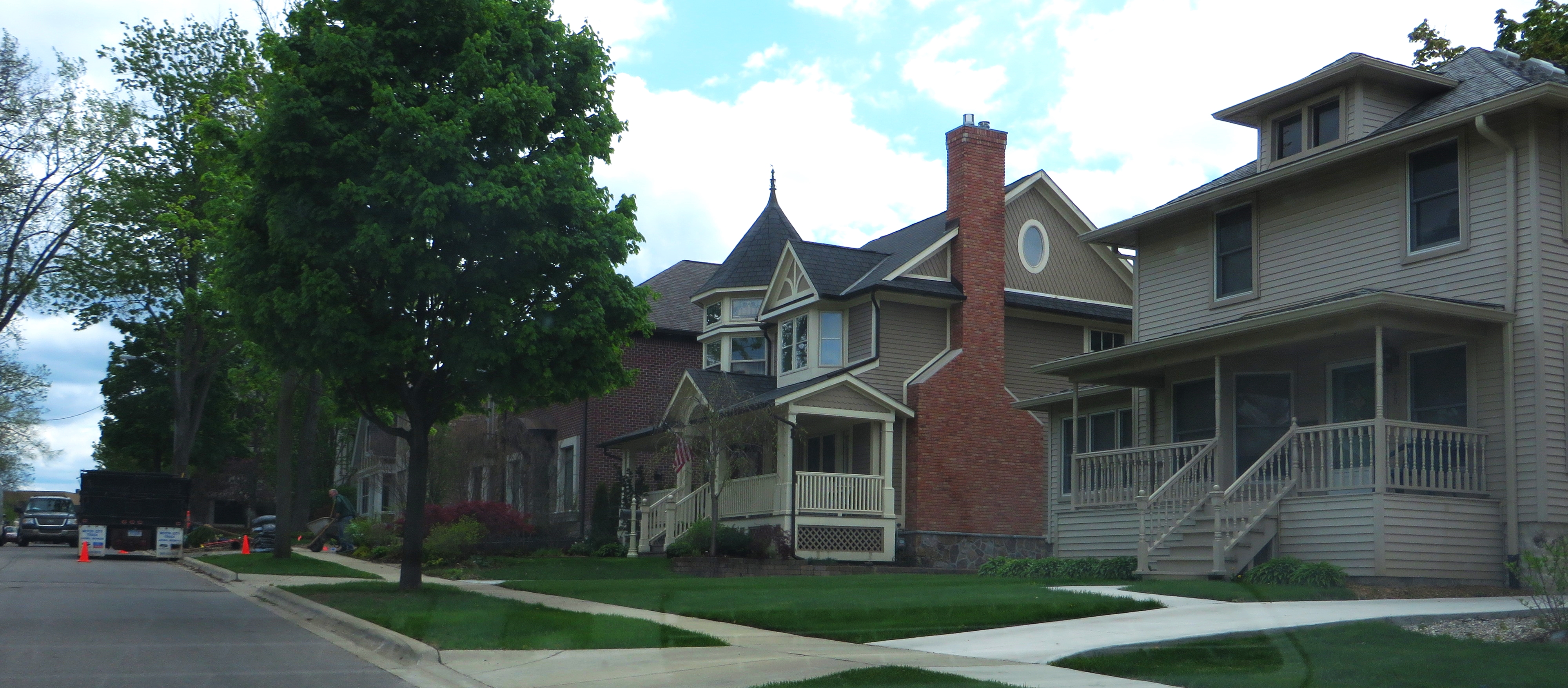 Tree-lined residential street with two-story single-family homes and green lawns.