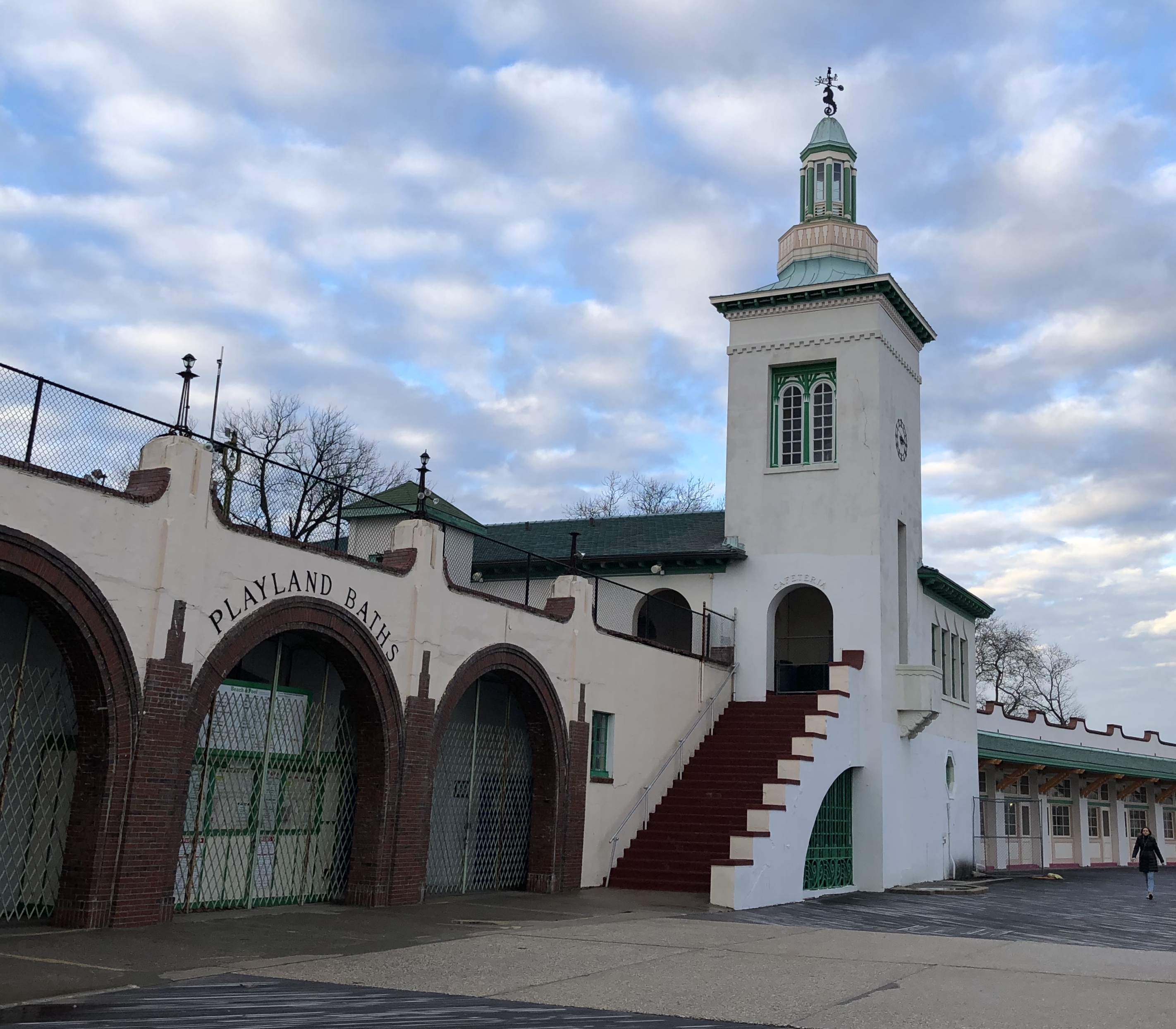 White stucco tower with green copper cupola and arched gated entrances.