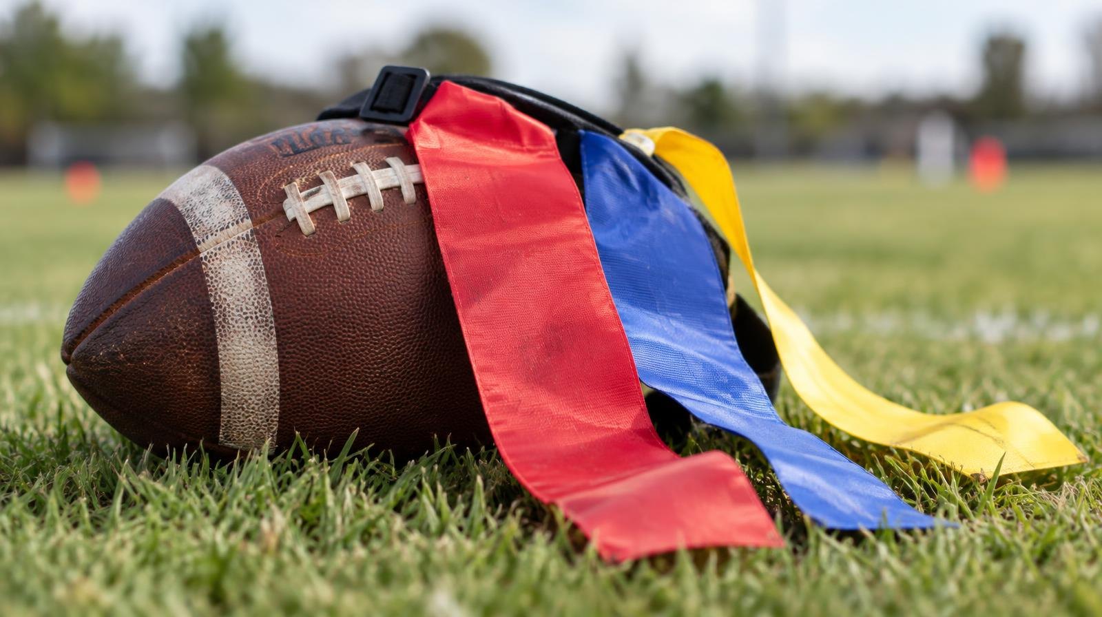 A football with colorful flag football belts draped over it on green grass.