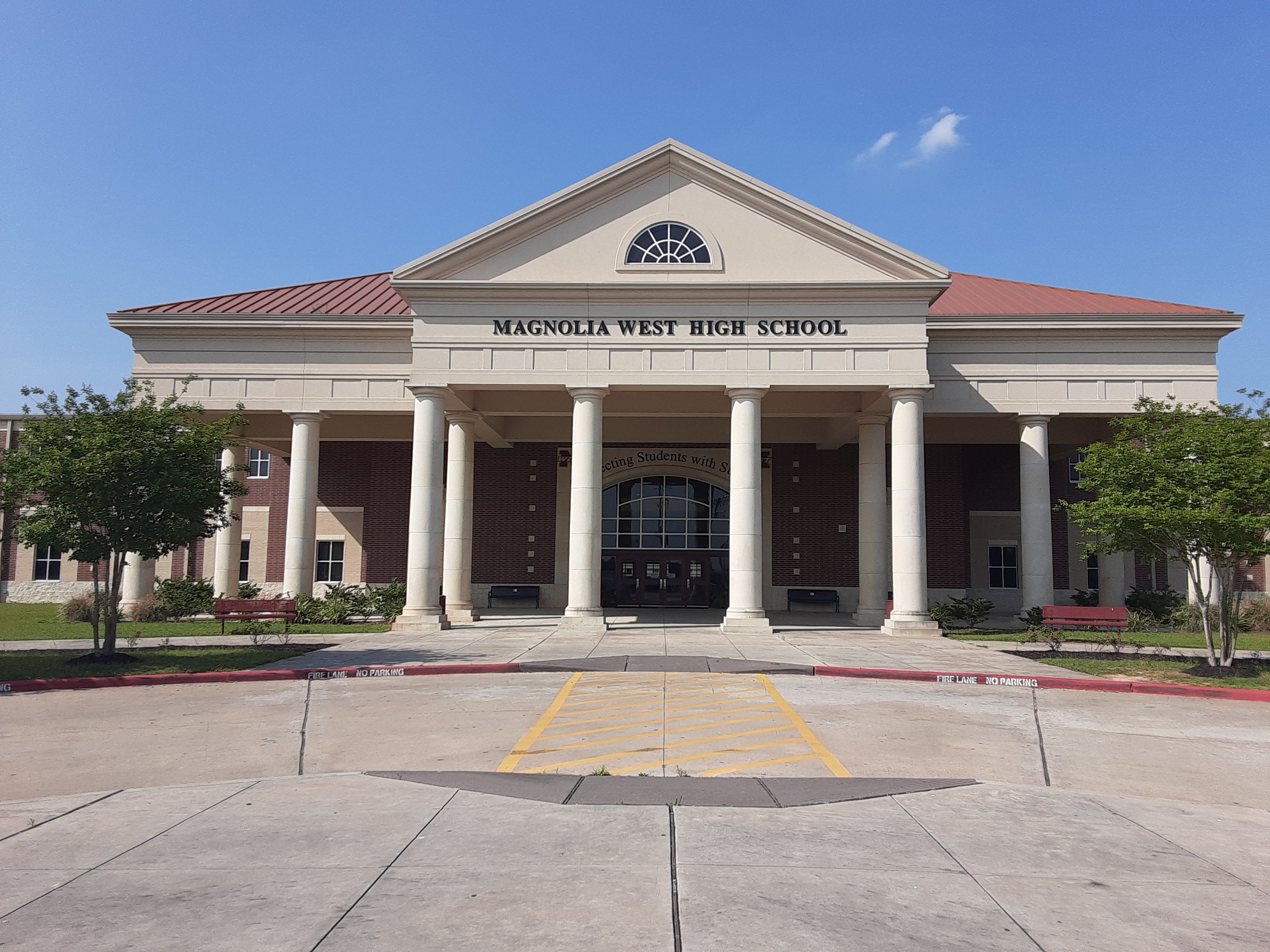 Brick school building with white columns and red-roofed entrance under a clear blue sky.