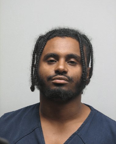 Booking-style portrait of a young man with braided hair and a short beard.