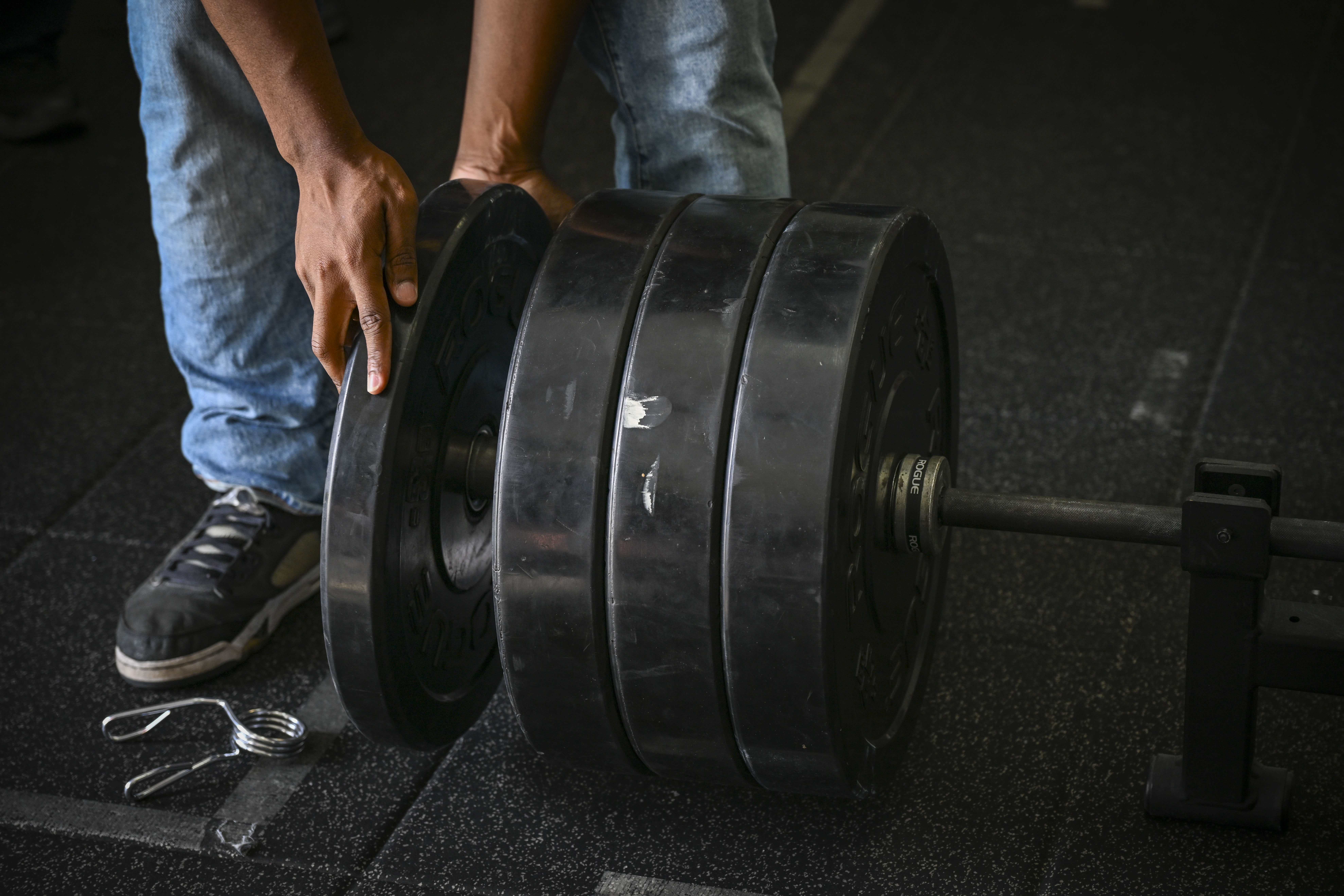 Hands loading large black weight plates onto a barbell on a gym floor.