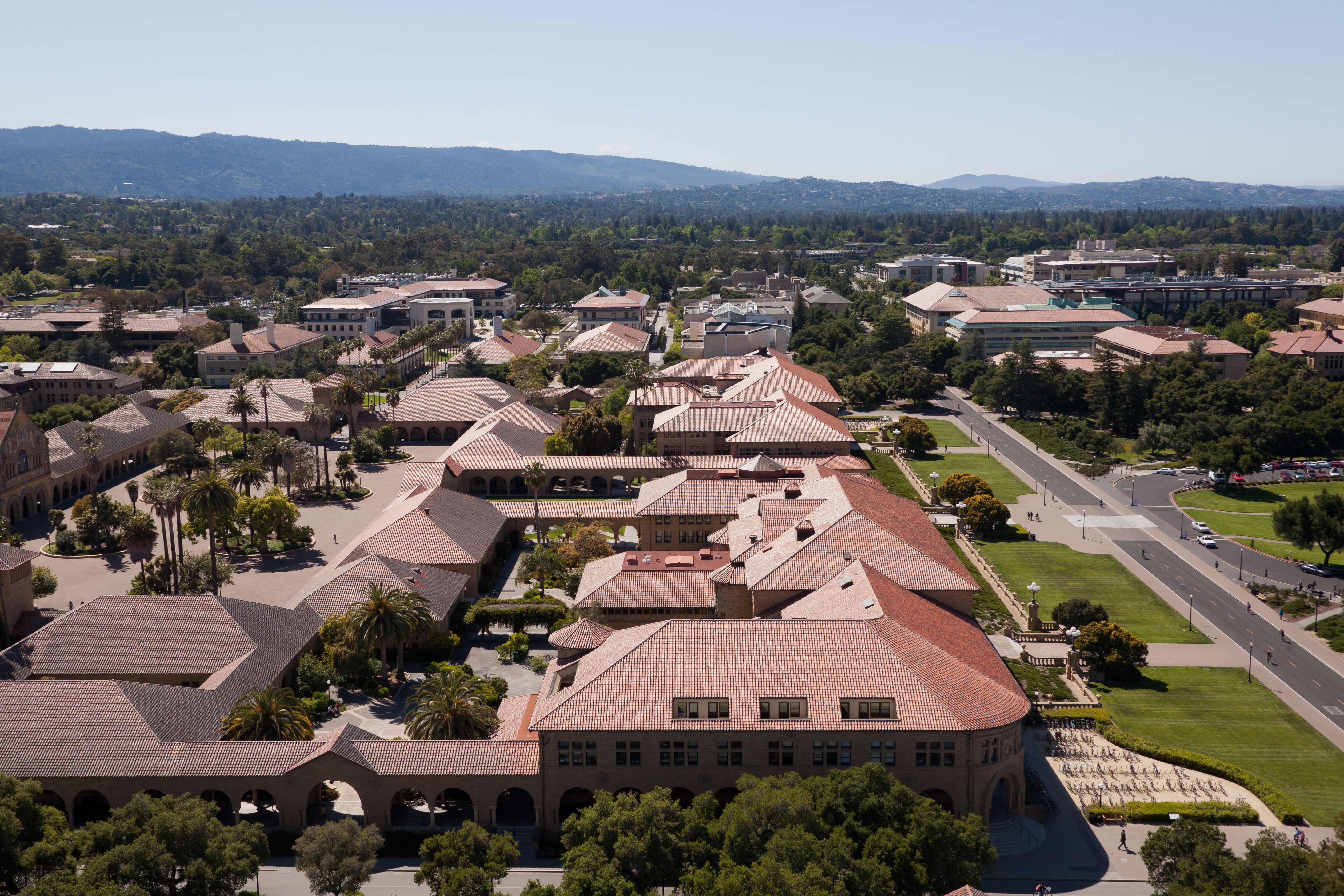 Aerial view of a university campus with red-tiled roofs, palm trees, and distant mountains.