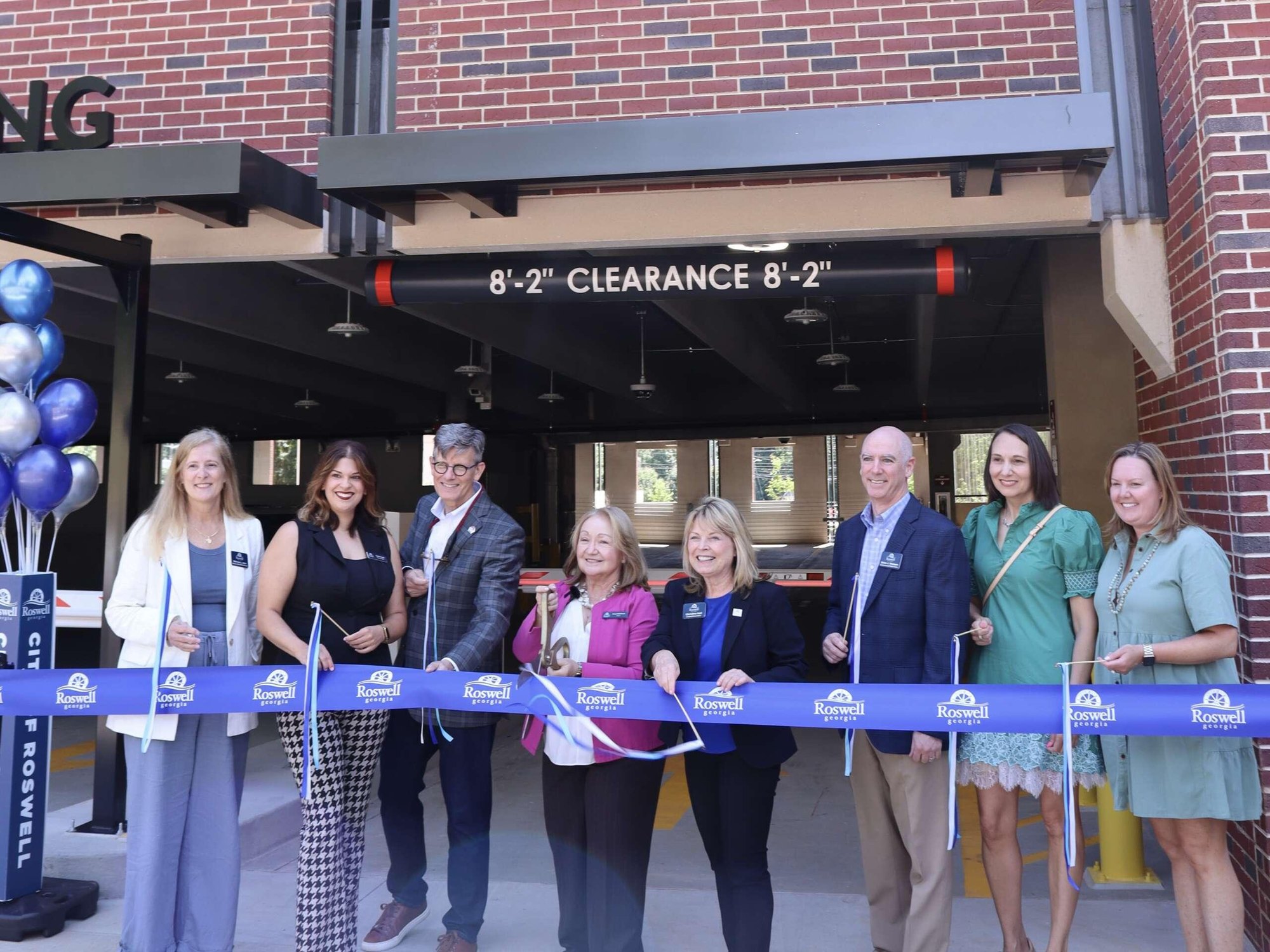 Group of people cutting a blue Roswell-branded ribbon at a parking structure entrance.