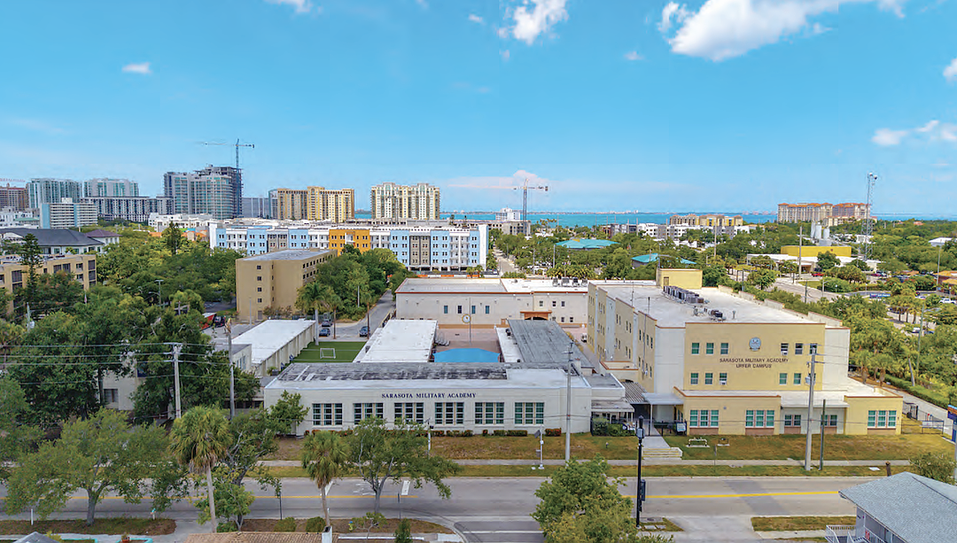 Aerial photo of a school campus with courtyards and athletic areas surrounded by mid-rise buildings.
