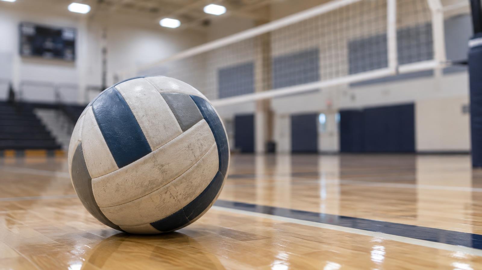 A volleyball resting on a hardwood gymnasium floor near a net.