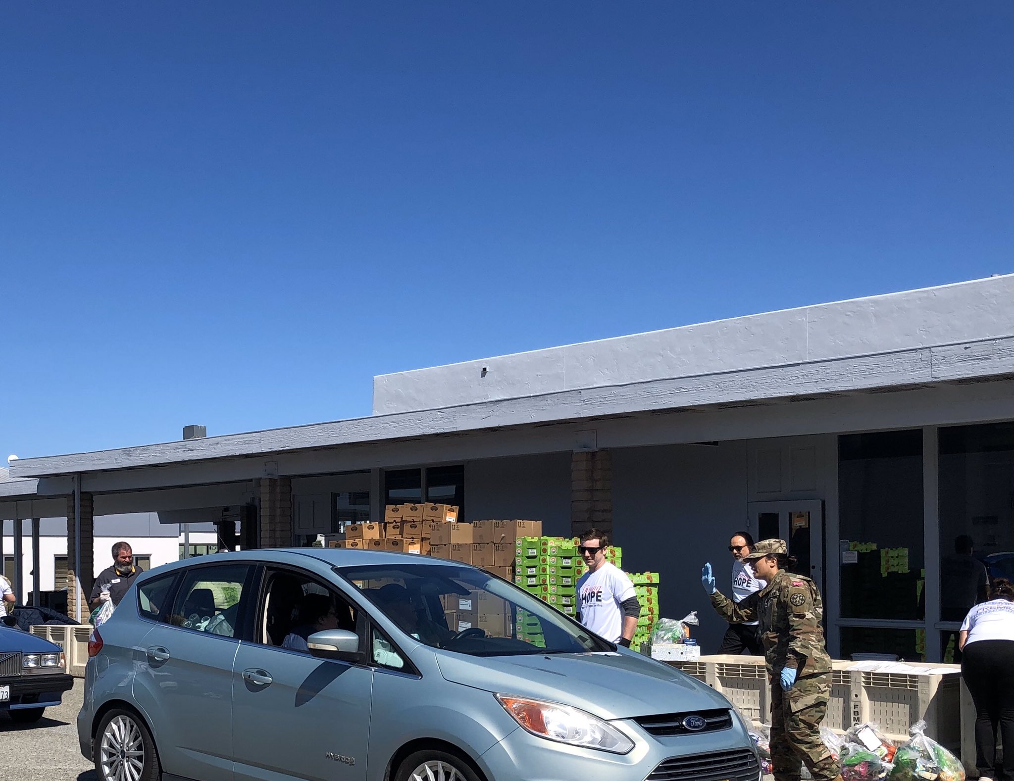 Volunteers hand boxes of produce to people in cars at a drive-through food distribution event.