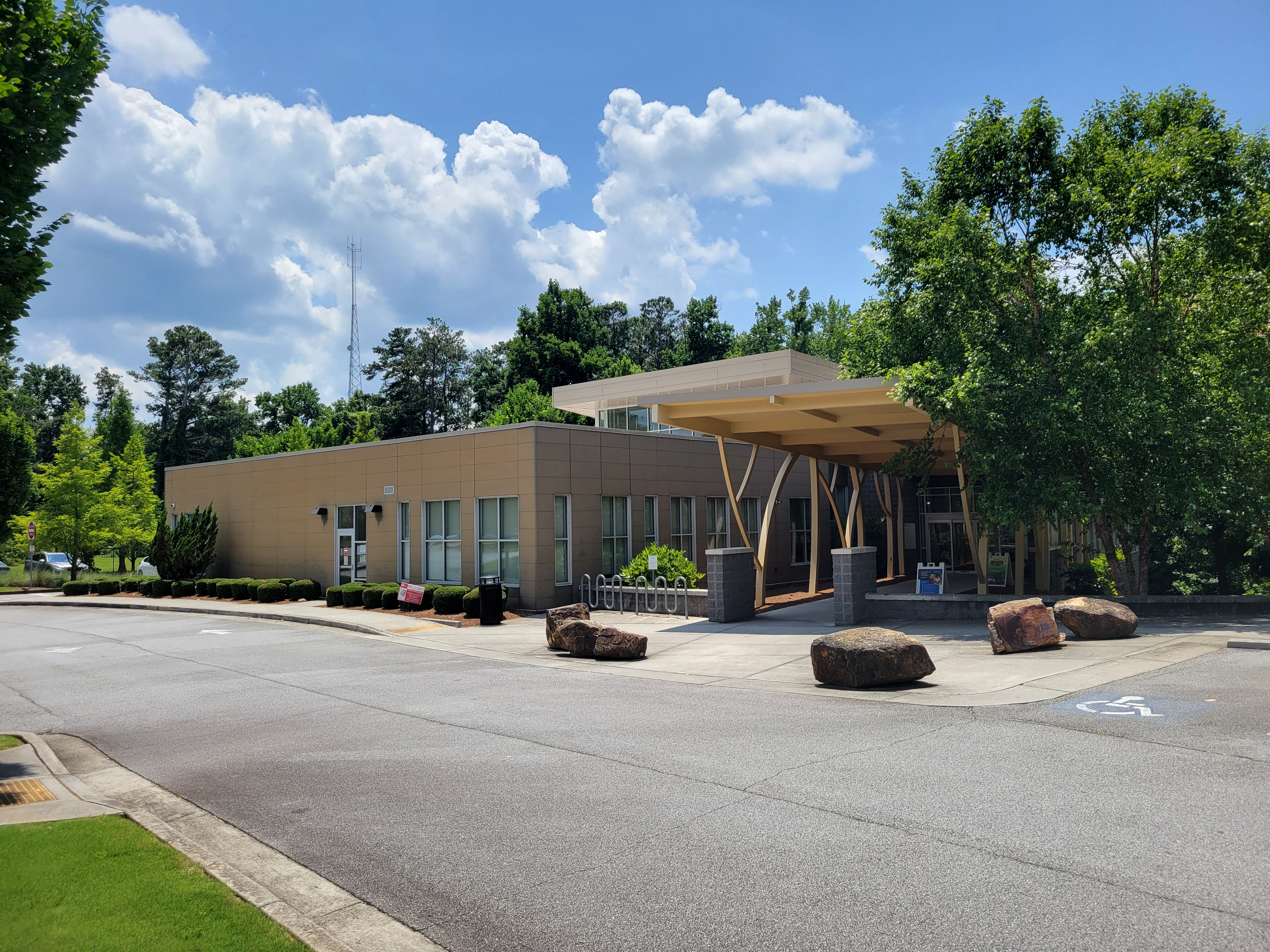 Modern single-story library building with a wooden canopy entrance and boulders in the foreground.